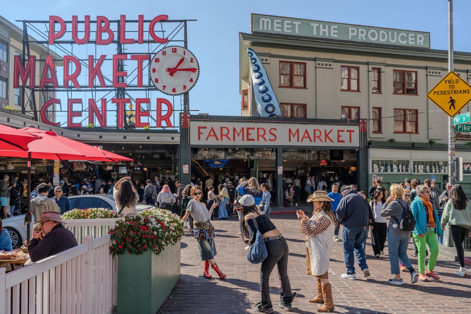 Crowds gather at Pike Place Public Market Center farmers market in Seattle on a sunny day.