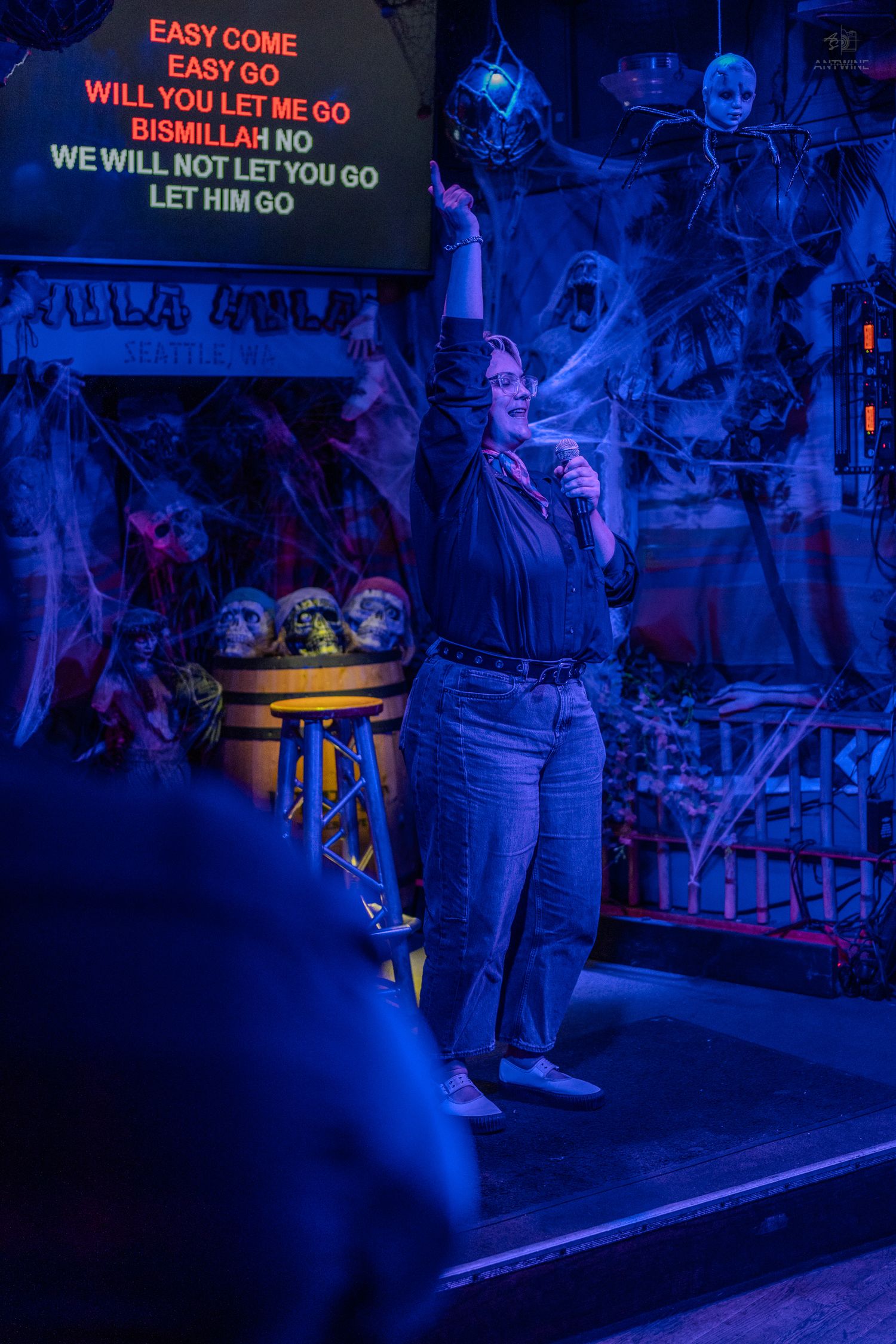 Singer performing Bohemian Rhapsody karaoke with arm raised on Halloween-themed stage at Hula Hula.