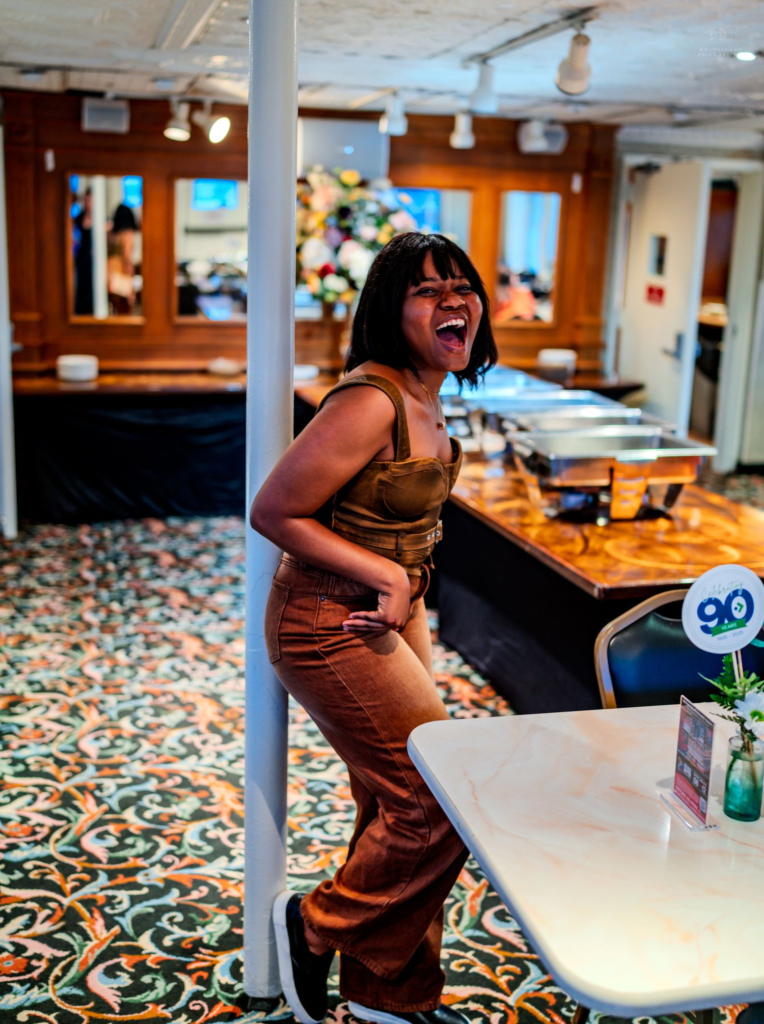 A joyful woman laughing in a decorated restaurant interior with colorful patterned flooring.