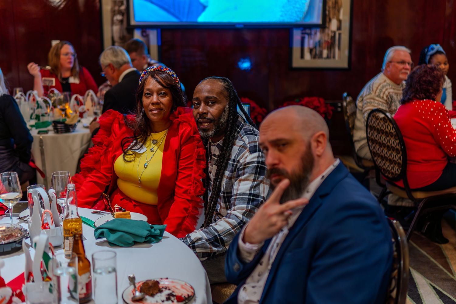 People smiling and posing at a festive holiday dinner event in an elegant banquet hall.