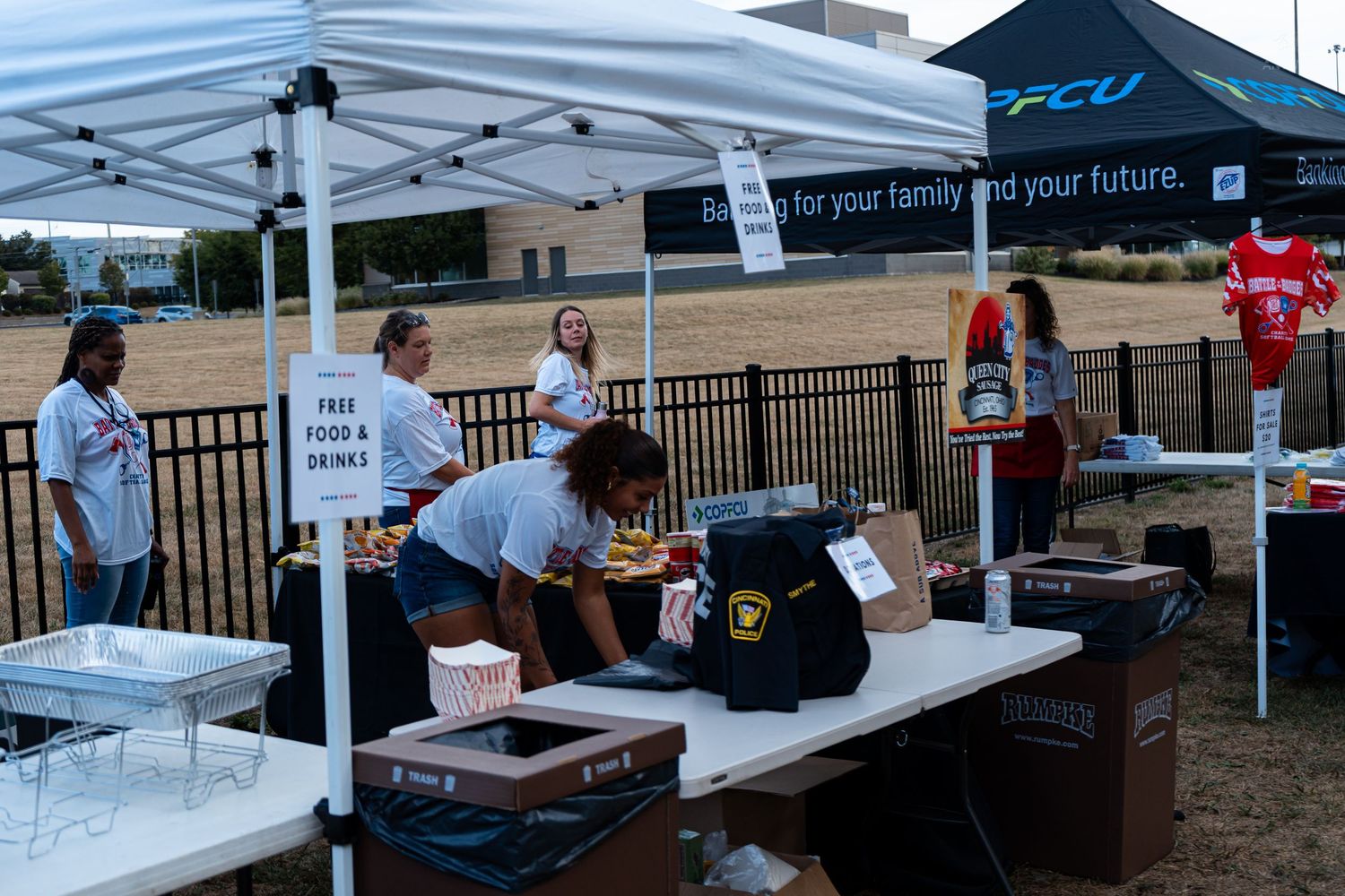 Volunteers serve free food and drinks under a tent at a charity outdoor community event.