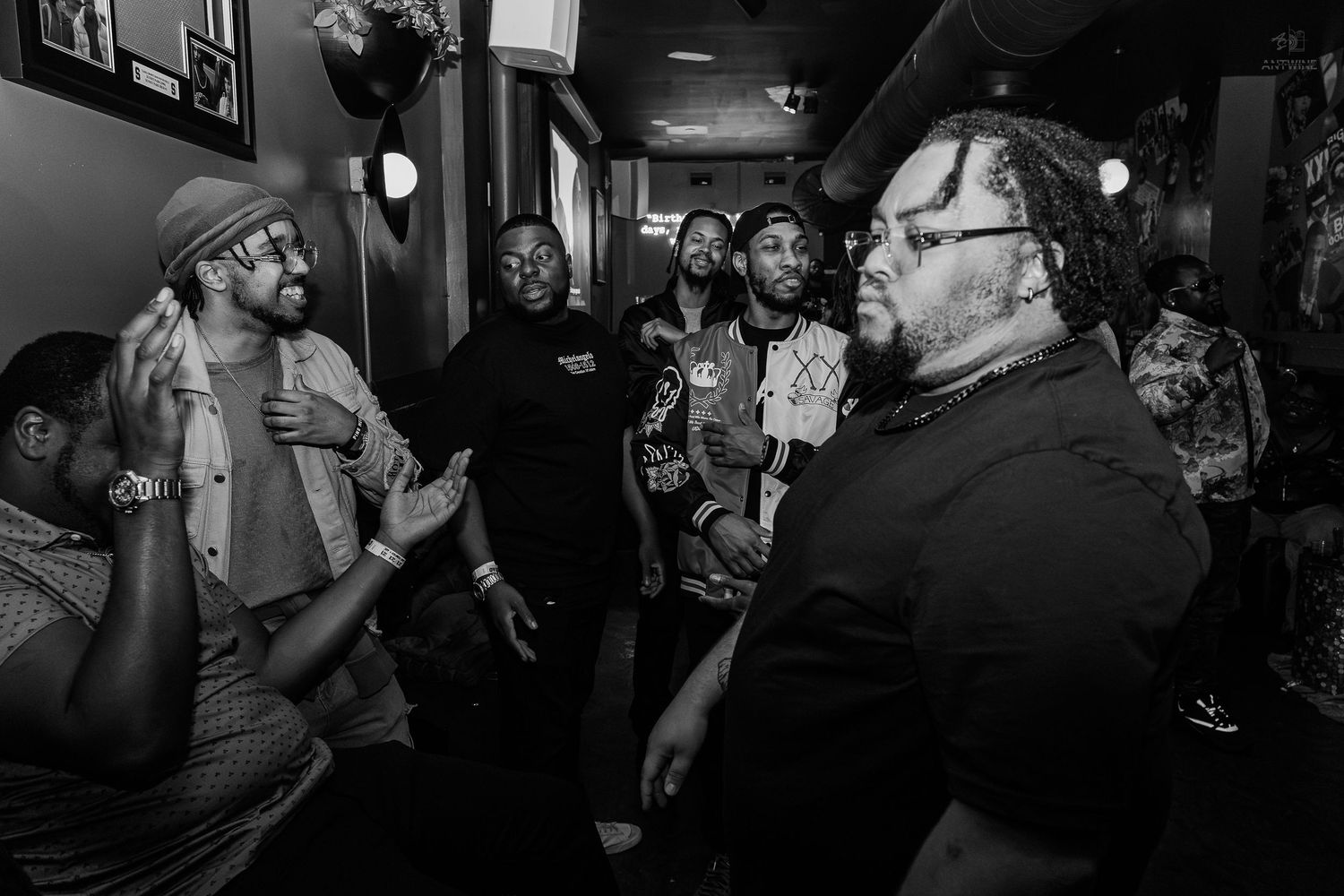 Black and white photo of a group of men gathered in a hallway, engaged in lively conversation at a social event.