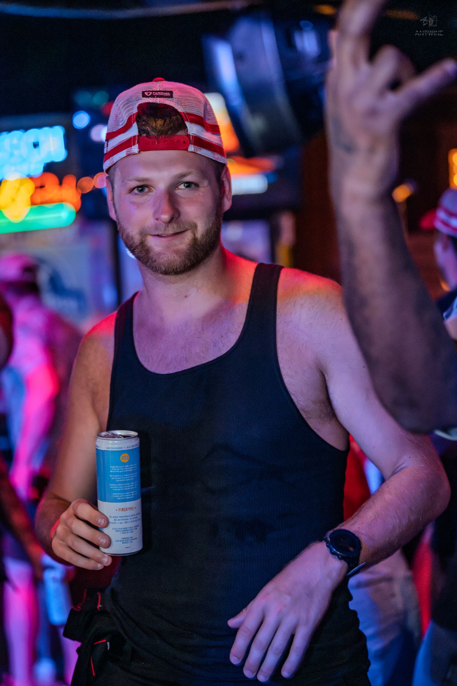 Young man in a red snapback cap holding a canned drink at a neon-lit bar.