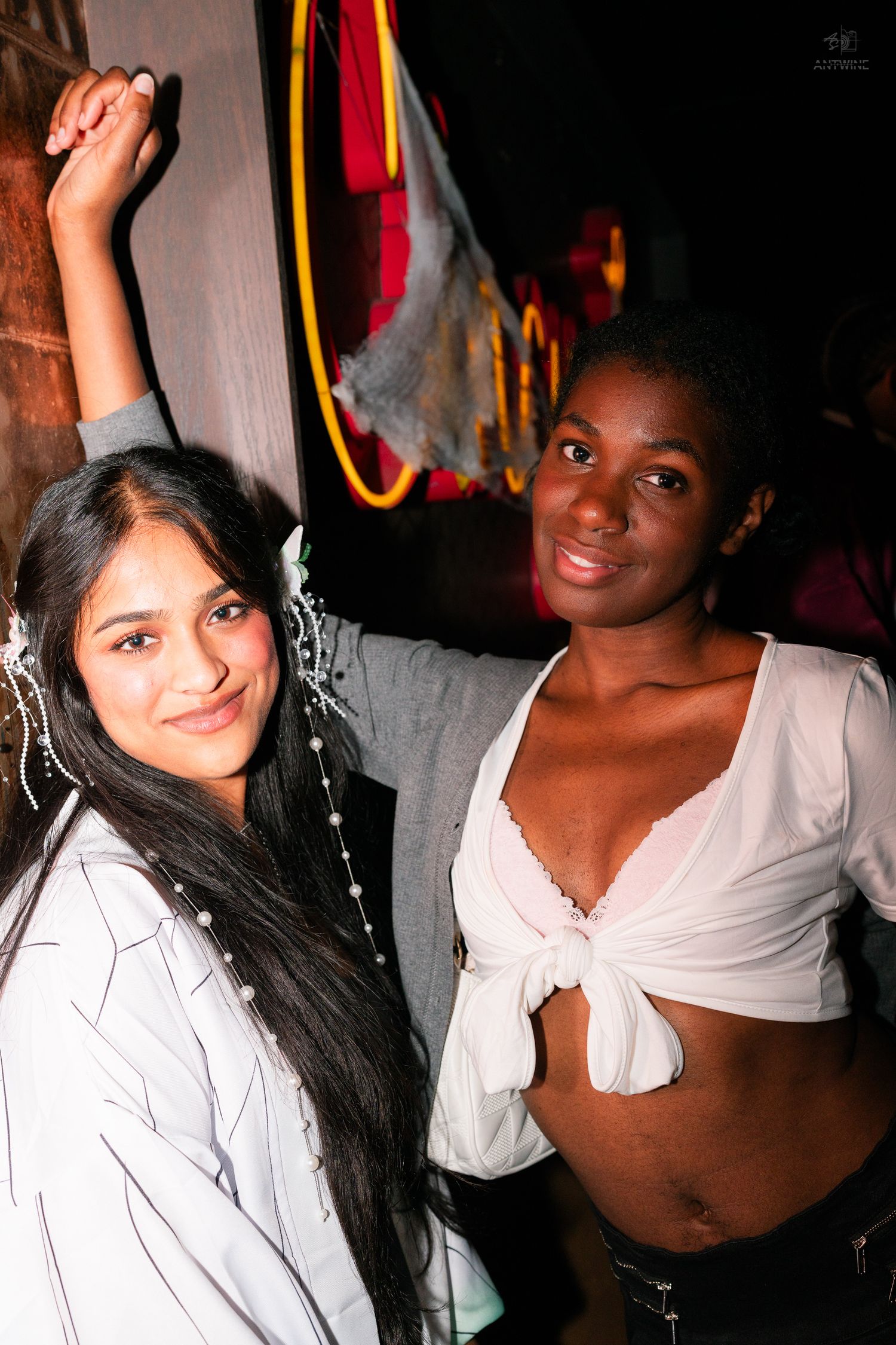 Two young women posing together at a Halloween nightclub party, one in bridal costume with pearl accessories.
