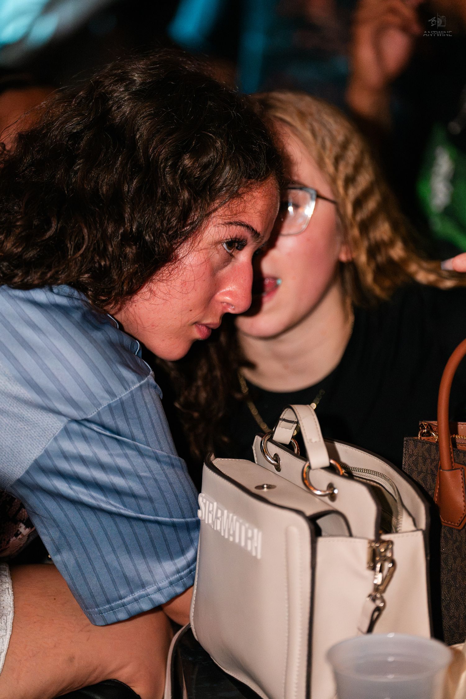 Two women having a close conversation at a dimly lit nightclub party.