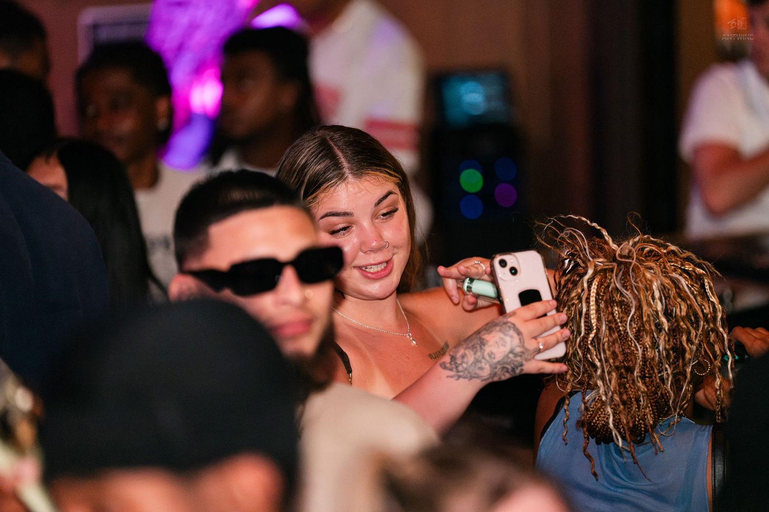 Woman smiling while taking a selfie with a friend at a crowded party.