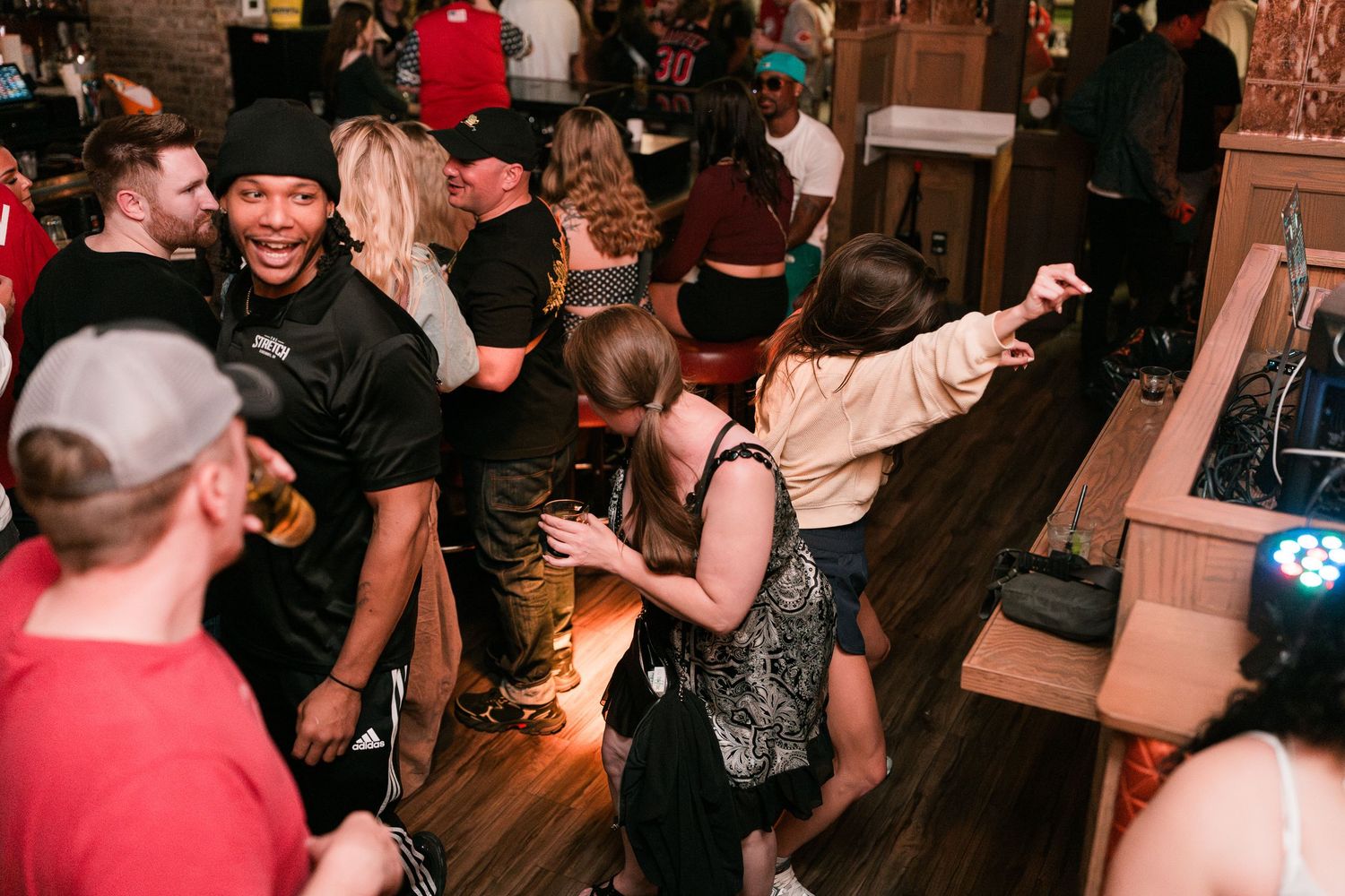 A diverse group of people dancing and having fun on a crowded bar dance floor with colorful lights.