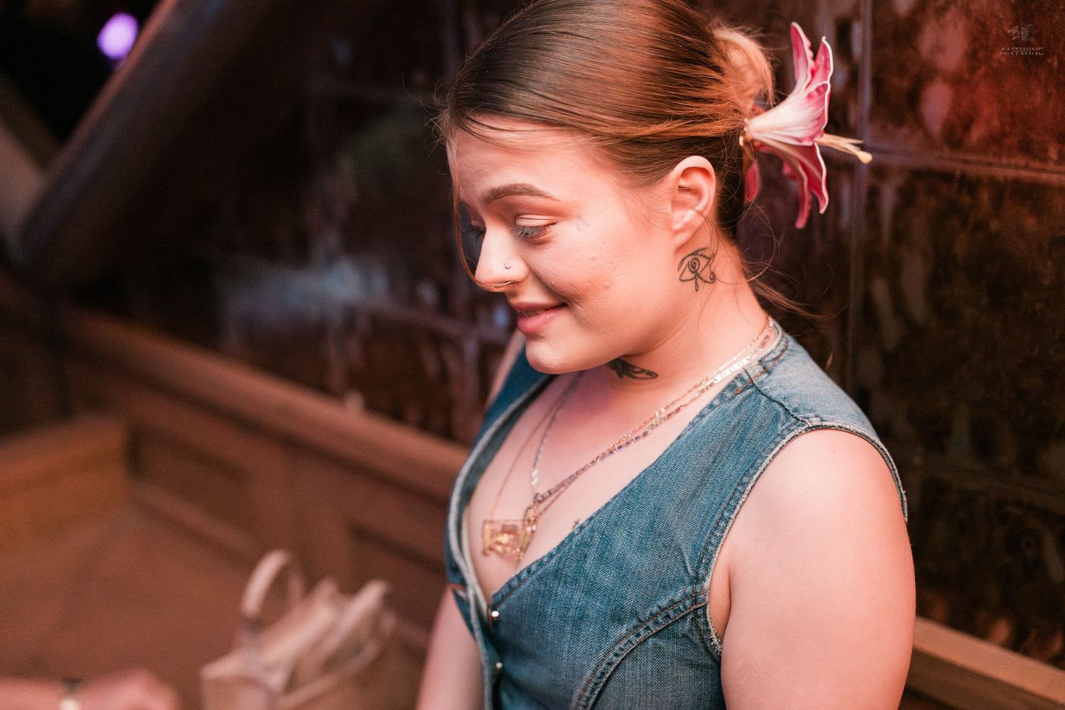 Young woman with floral hair accessory and denim top smiling at a dimly lit bar.