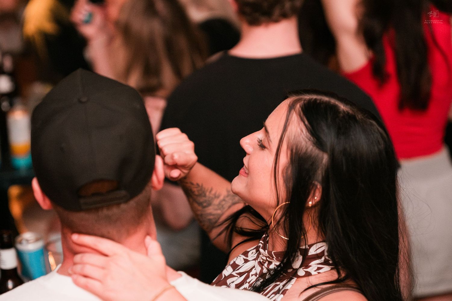 Woman with dark hair dances closely with a man in a black cap at a nightclub.