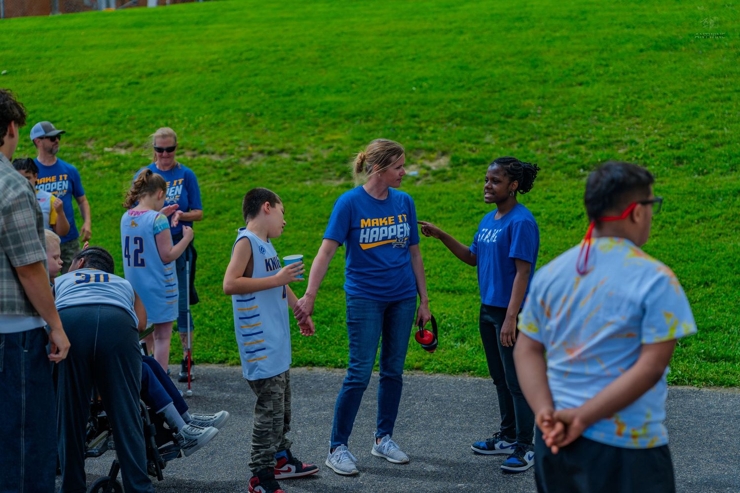 Group of kids and adults in blue shirts socializing outdoors on a green lawn during a community event.