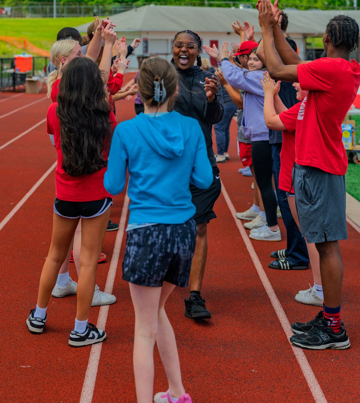 Students form a celebratory high-five tunnel on a red track during a school field day event.