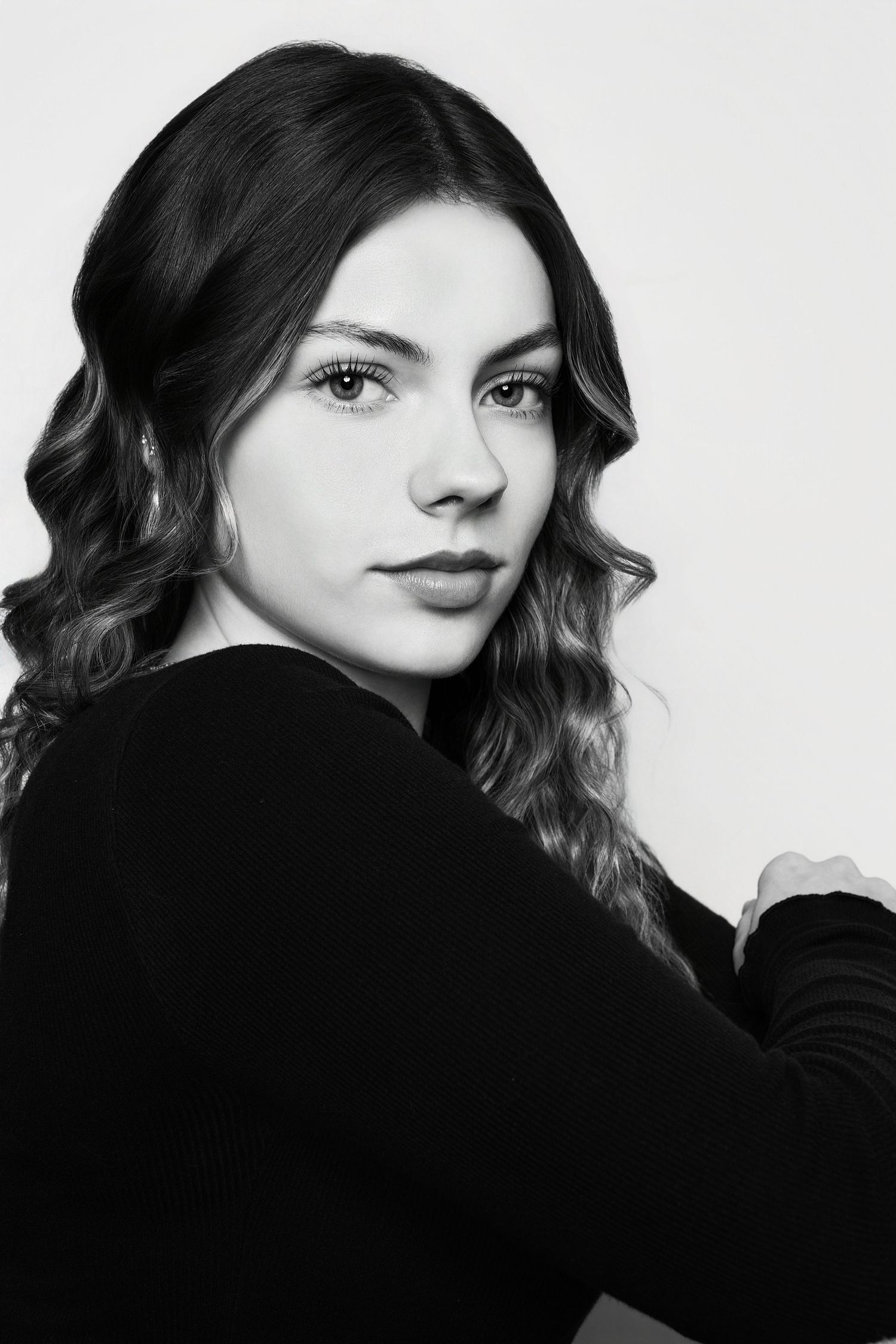 Elegant black and white studio portrait of a young woman with curly hair wearing a black long-sleeve top.