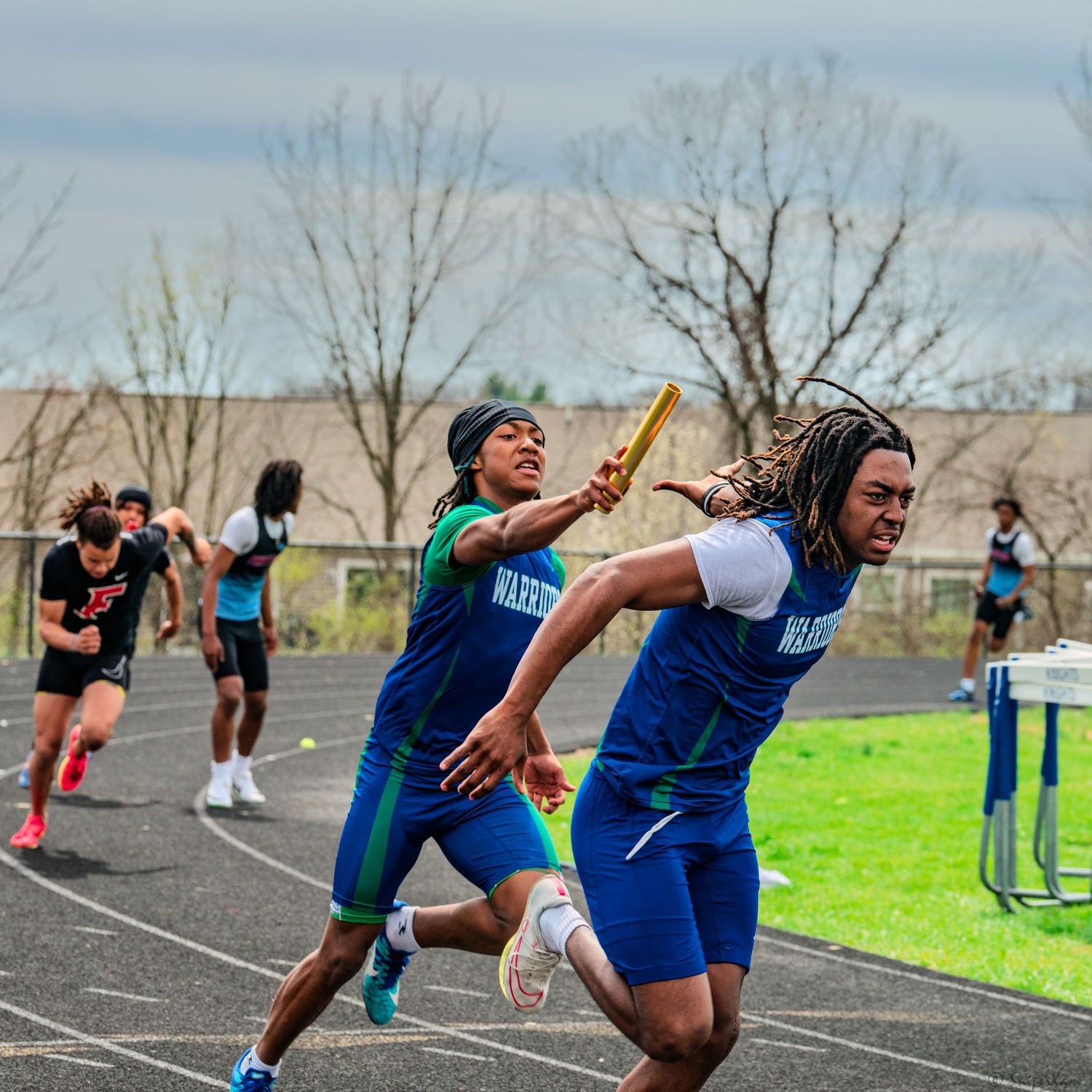 Warriors relay team passing baton during a competitive high school track and field relay race.