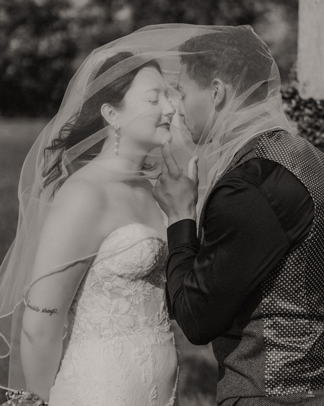Black and white romantic photo of bride and groom sharing an intimate moment under a wedding veil.