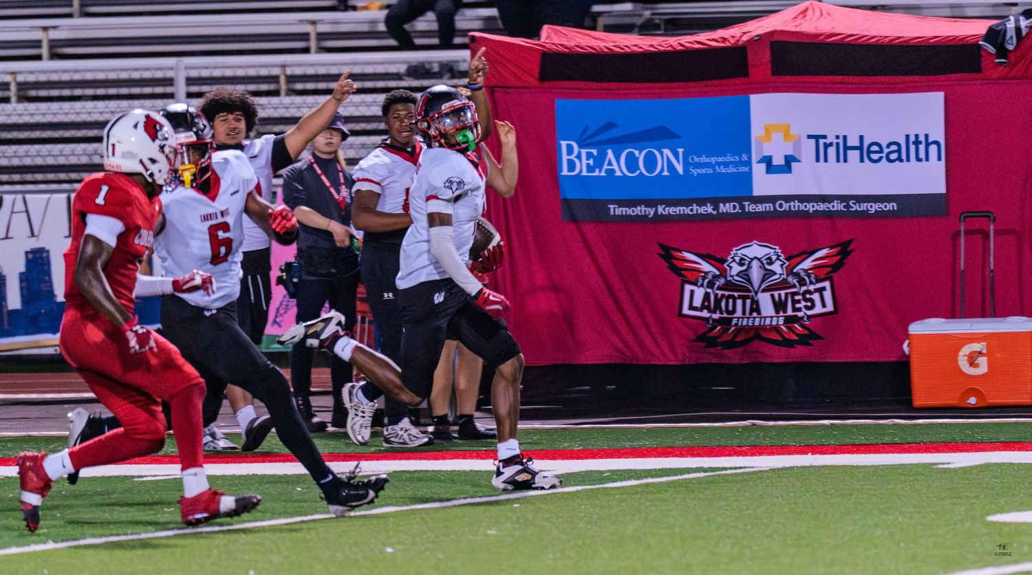 High school football players in red uniforms sprint along sideline during a competitive game.