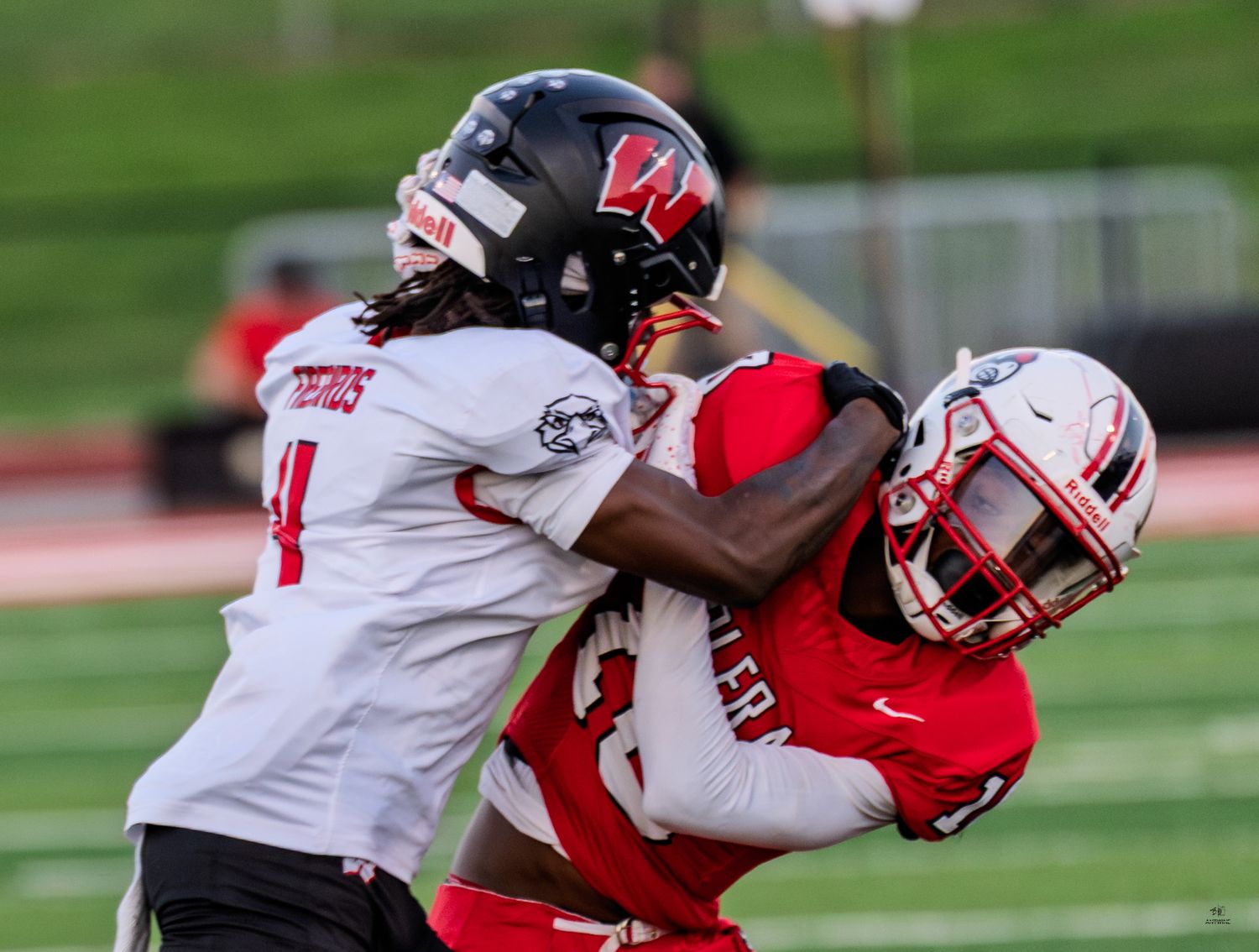 Two football players in red and white uniforms battle for the ball during an intense high school game.