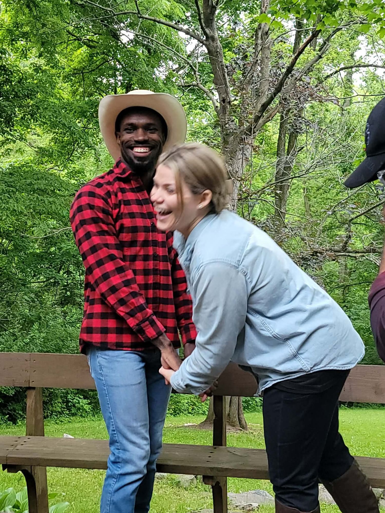 Two friends laughing and holding hands on a wooden deck surrounded by lush green trees outdoors.