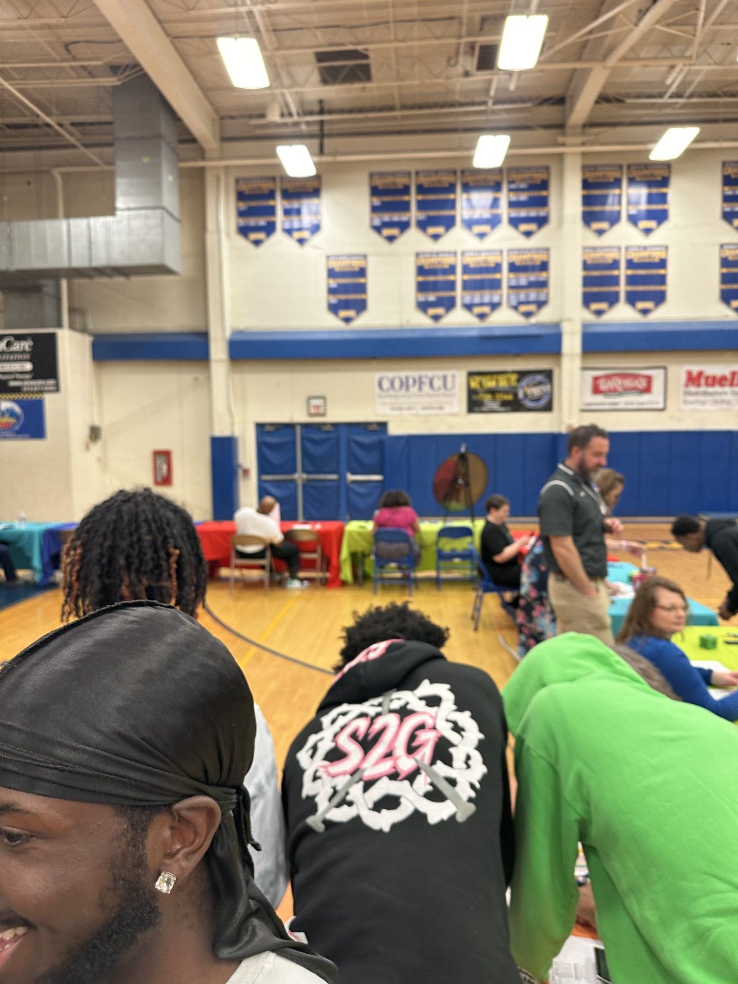 People gathered in a school gymnasium with championship banners on the wall during a community event.