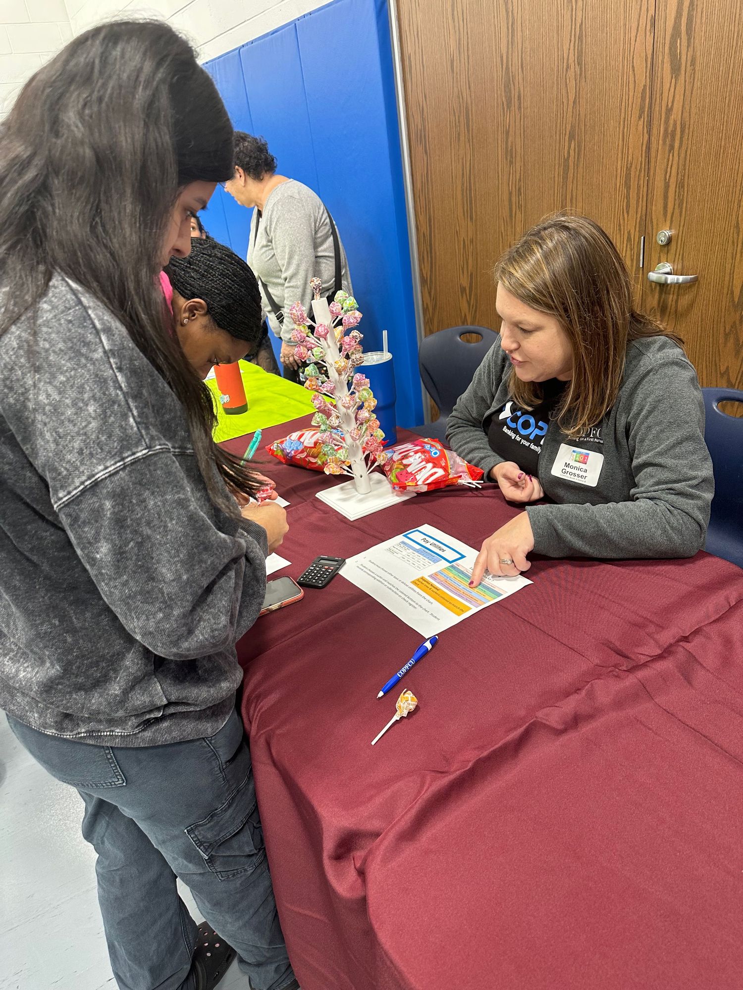 Students review a document with a female representative at a maroon-draped table adorned with a candy tree display.
