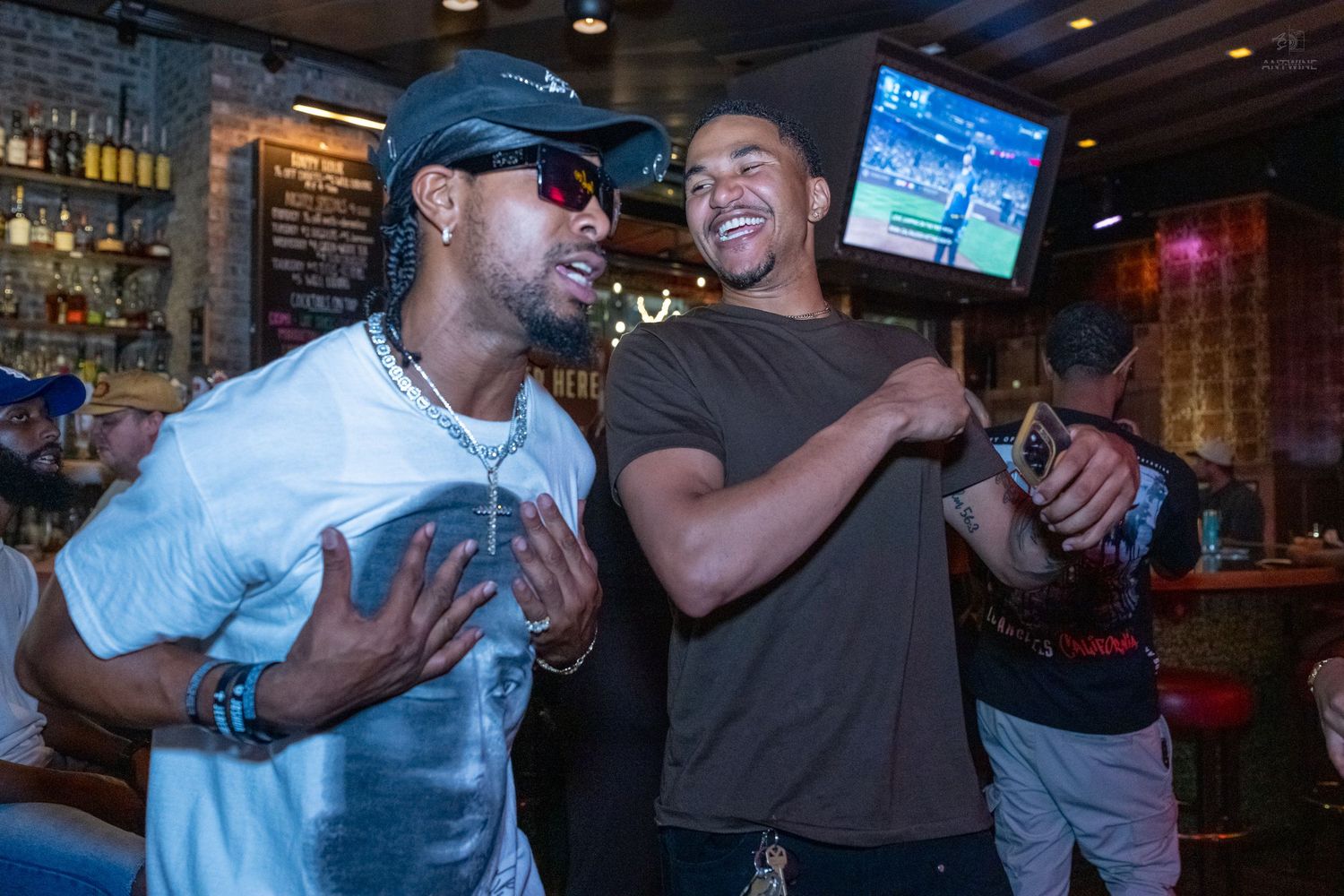 Two men laughing and taking a selfie together at a bar social event.