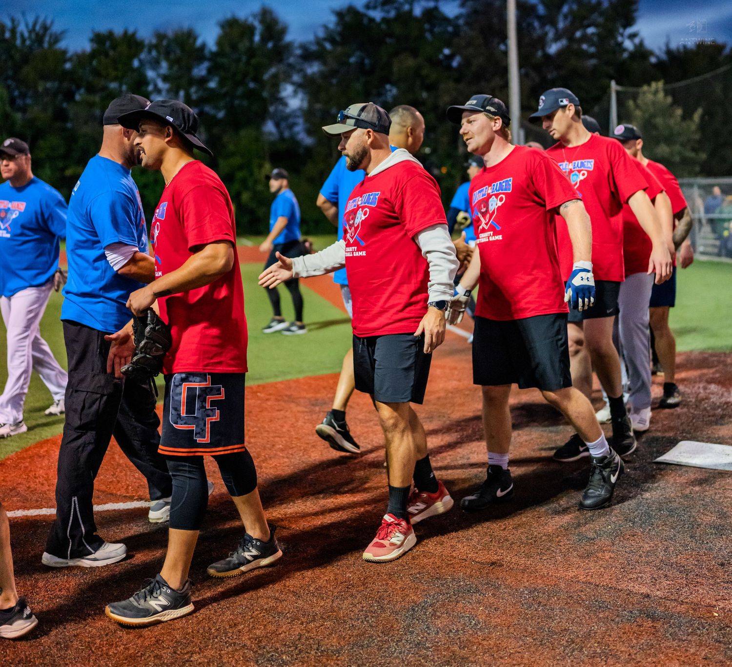 Teams shake hands on baseball field after game, players wearing red shirts with CF logo in evening light.