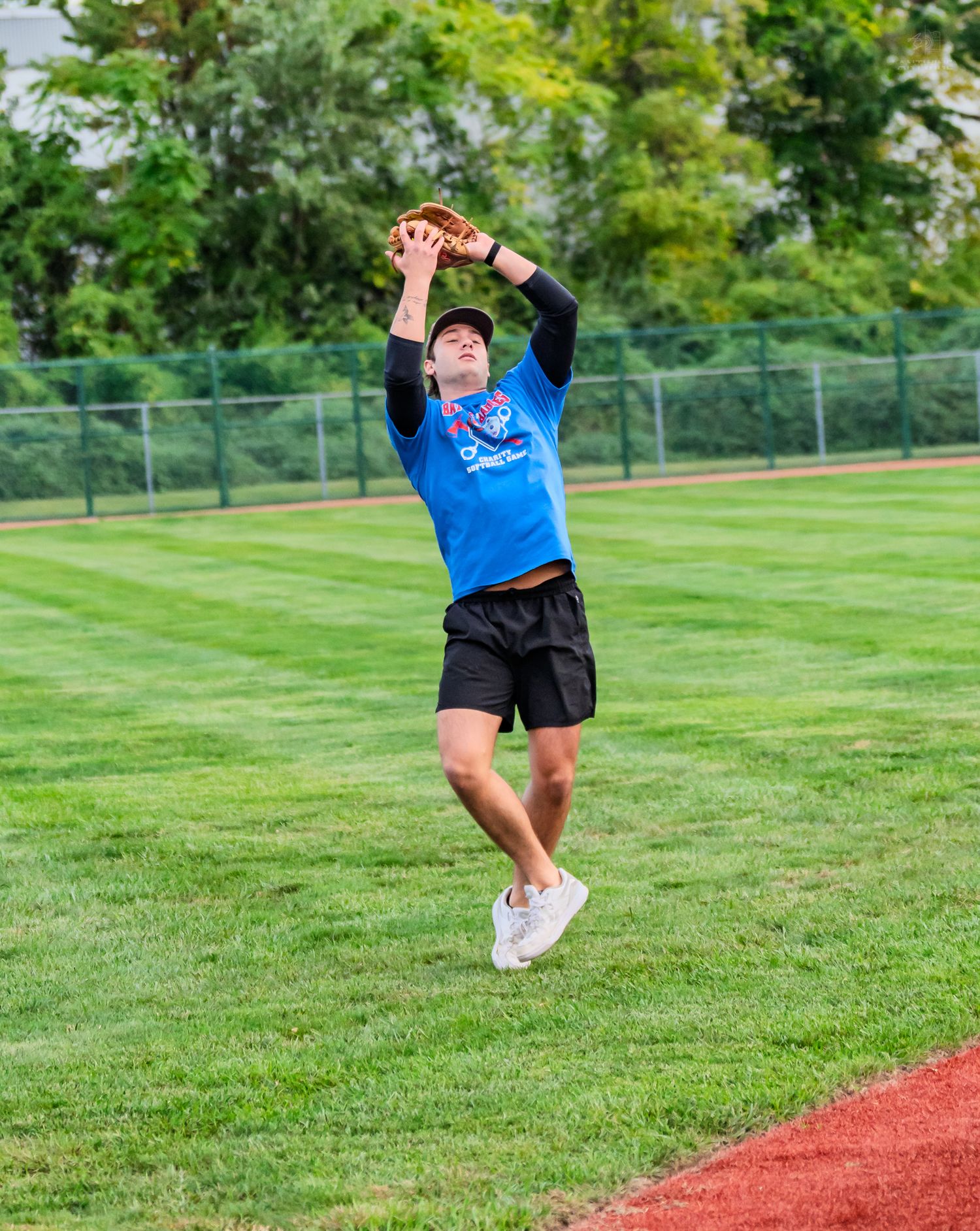 Baseball player in blue shirt catching a fly ball on a green grass field during a sunny day game.