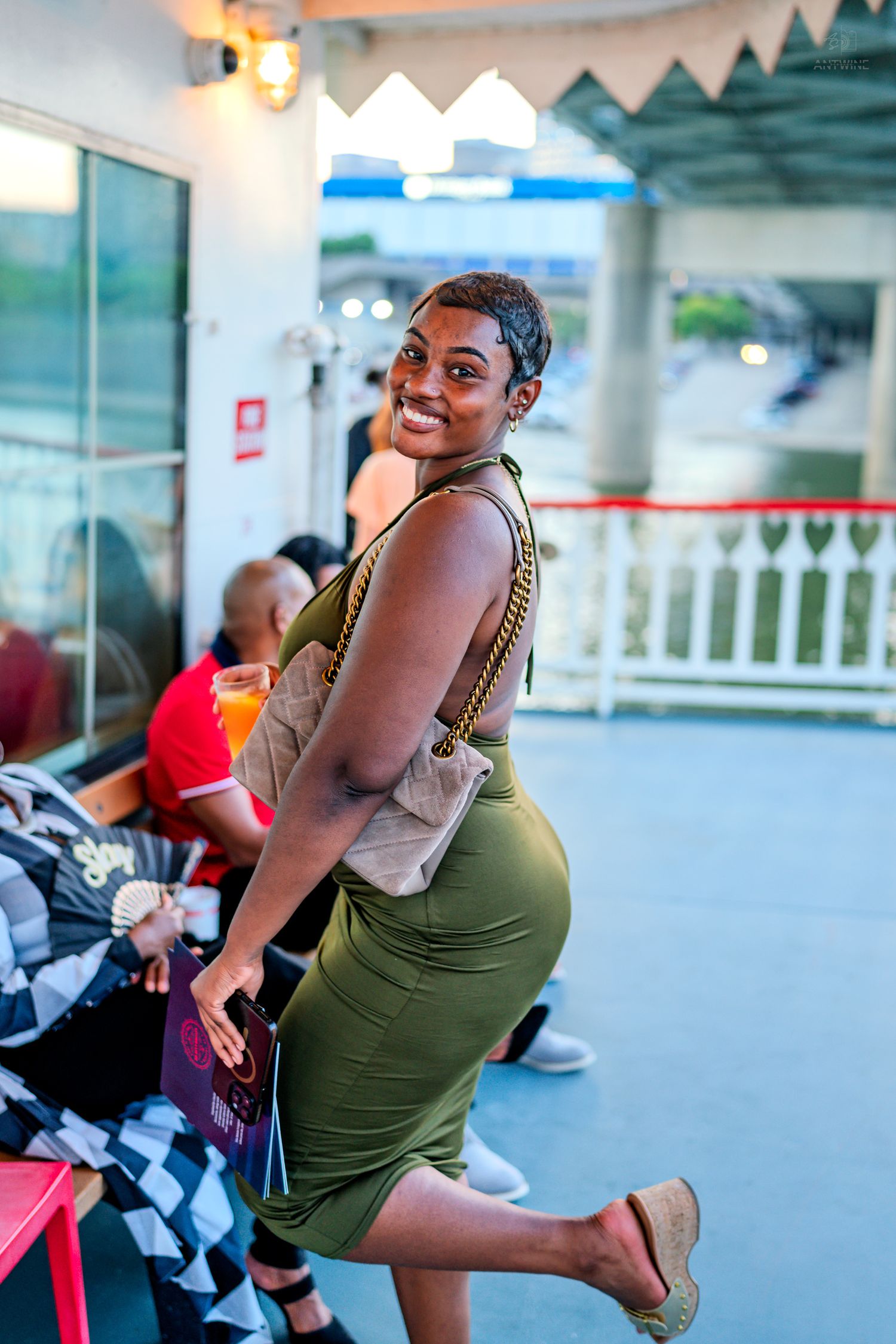 A smiling woman in an olive green dress poses on a riverboat deck at dusk.