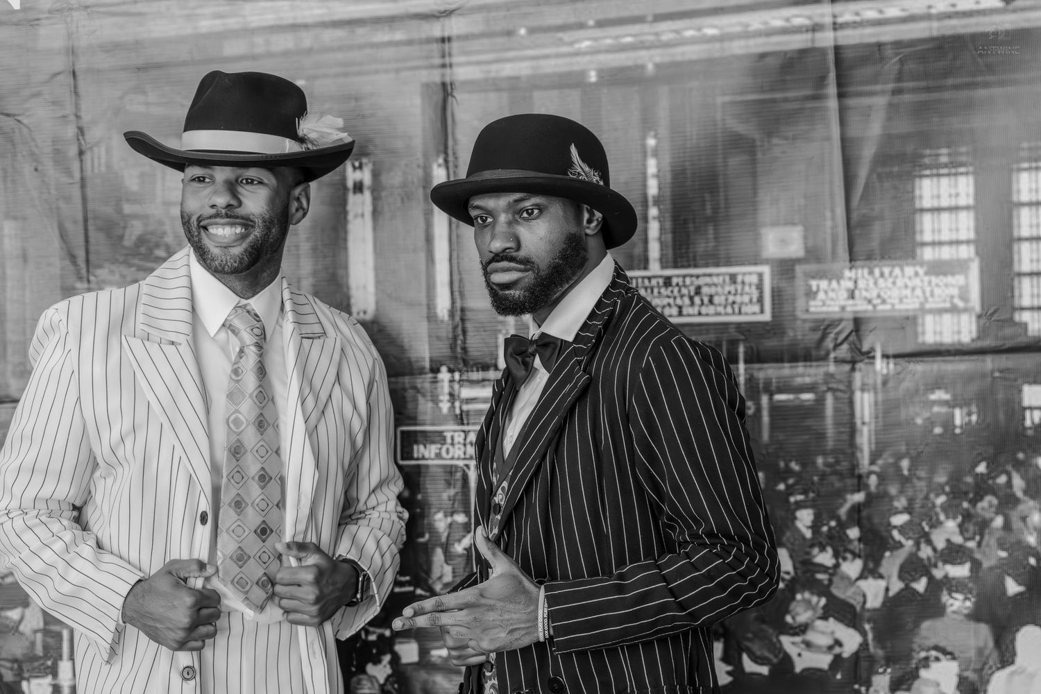 Two men in vintage pinstripe suits and hats pose elegantly in a black and white photo at a formal gathering.