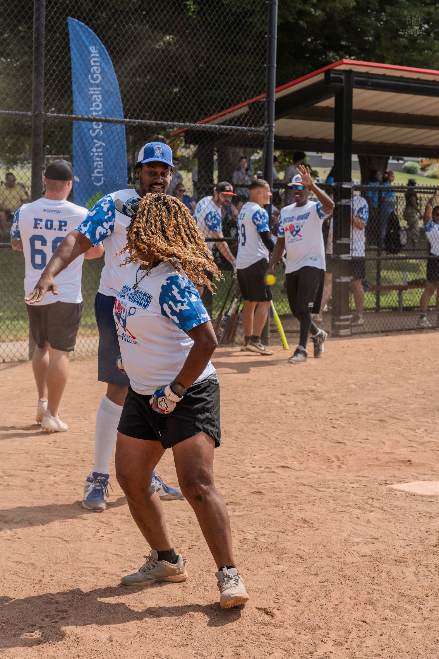 Energetic softball player with dreadlocks celebrating on the field at a charity softball game.