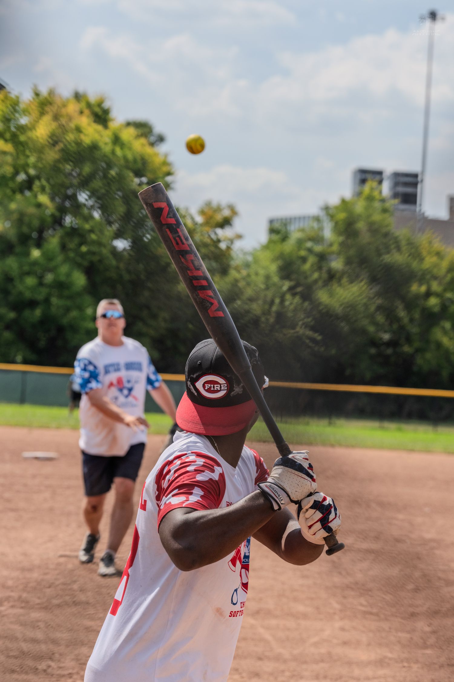 Baseball player in Local 48 jersey swinging at a yellow softball during an outdoor daytime game.