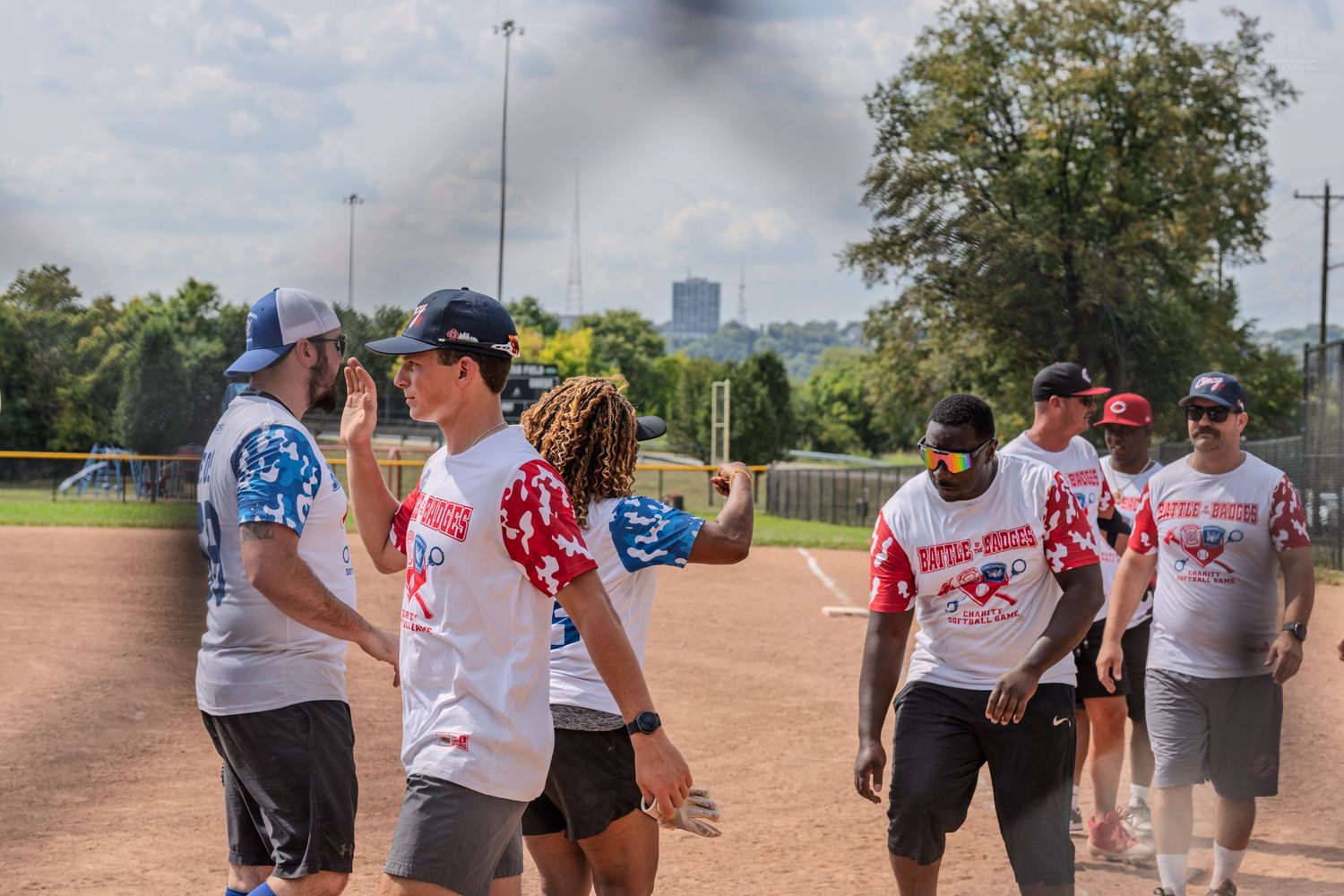 Softball players in red and white uniforms exchange high-fives on the field after a play.
