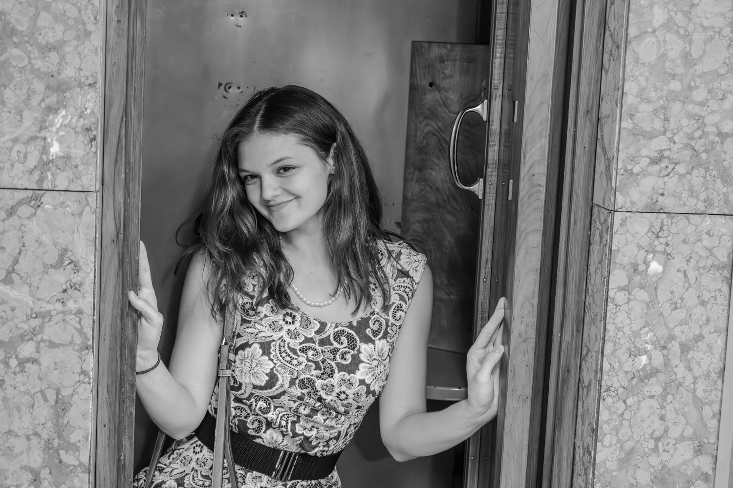 Young woman in floral dress making peace signs while posing in a doorway, black and white photo.
