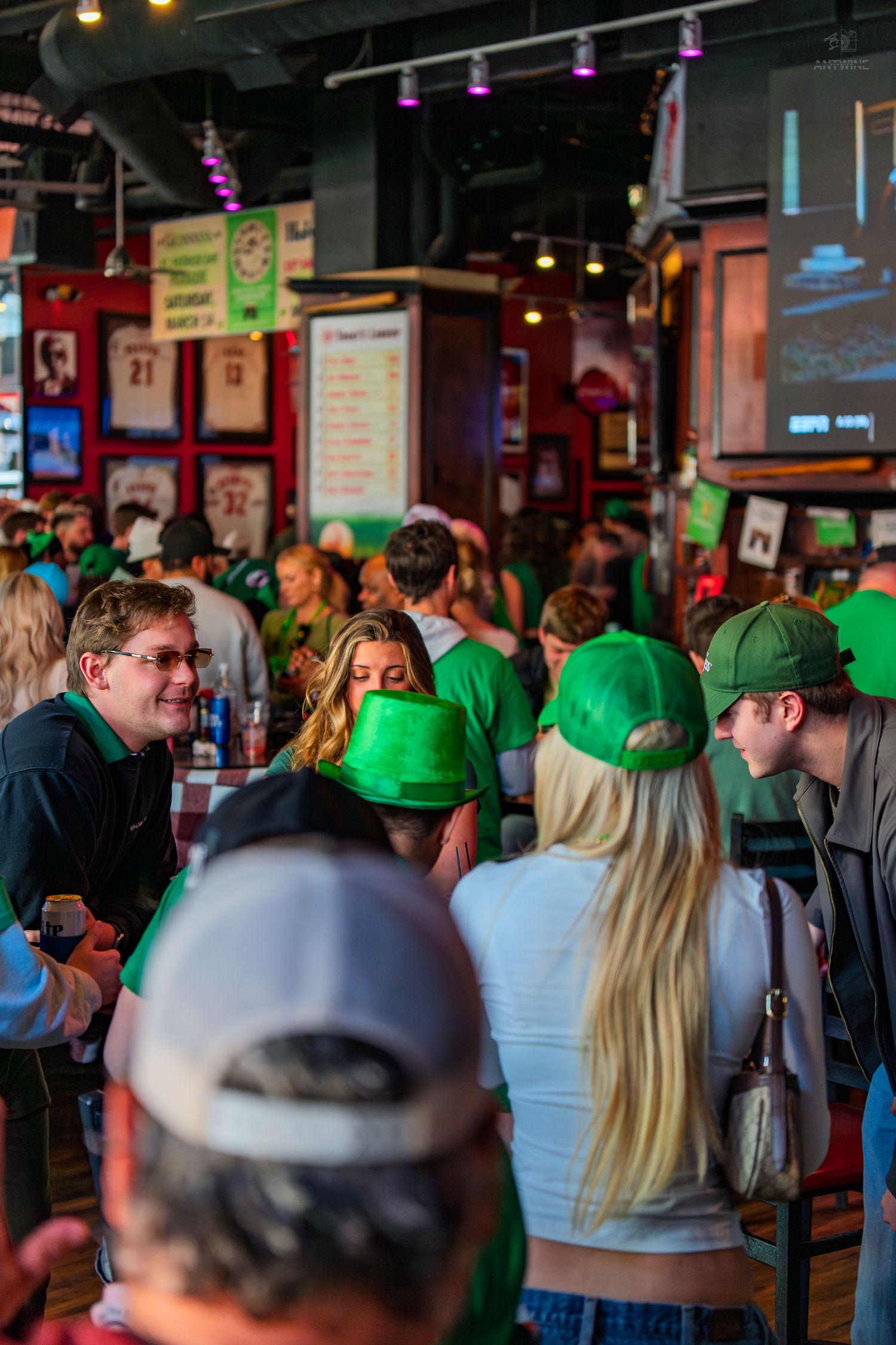Crowd of people wearing green celebrating St. Patrick's Day in a busy sports bar.