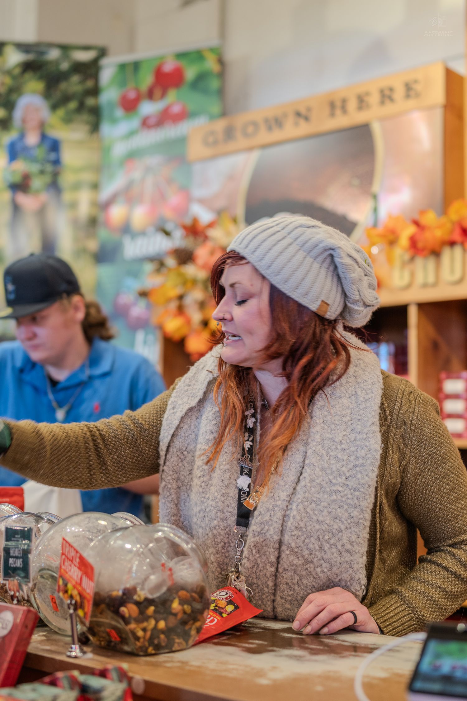 Woman in gray beanie hat shopping at a fall harvest market with a Grown Here banner in the background.