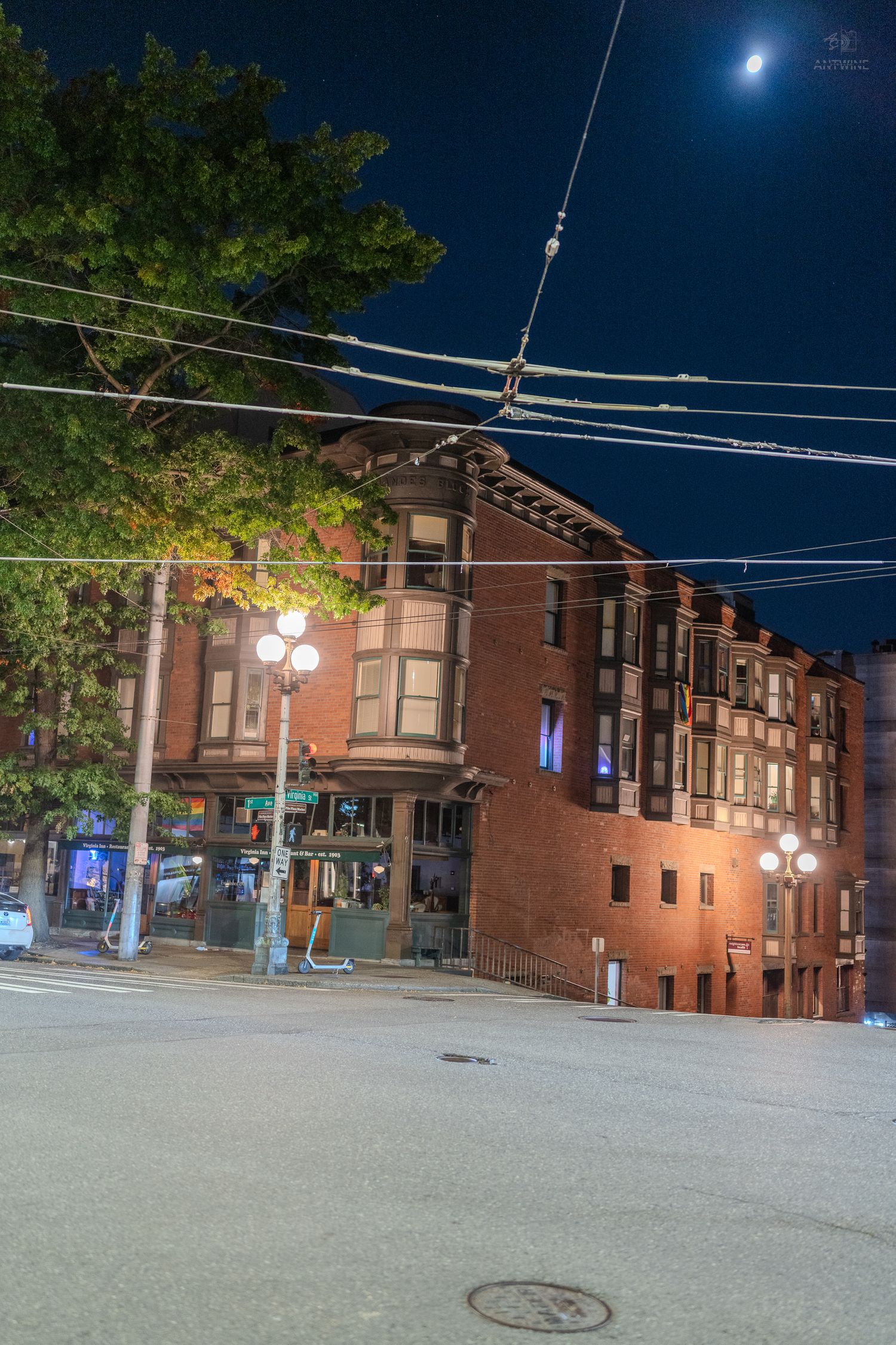Classic red brick Victorian building at night with moon visible in dark blue sky above.