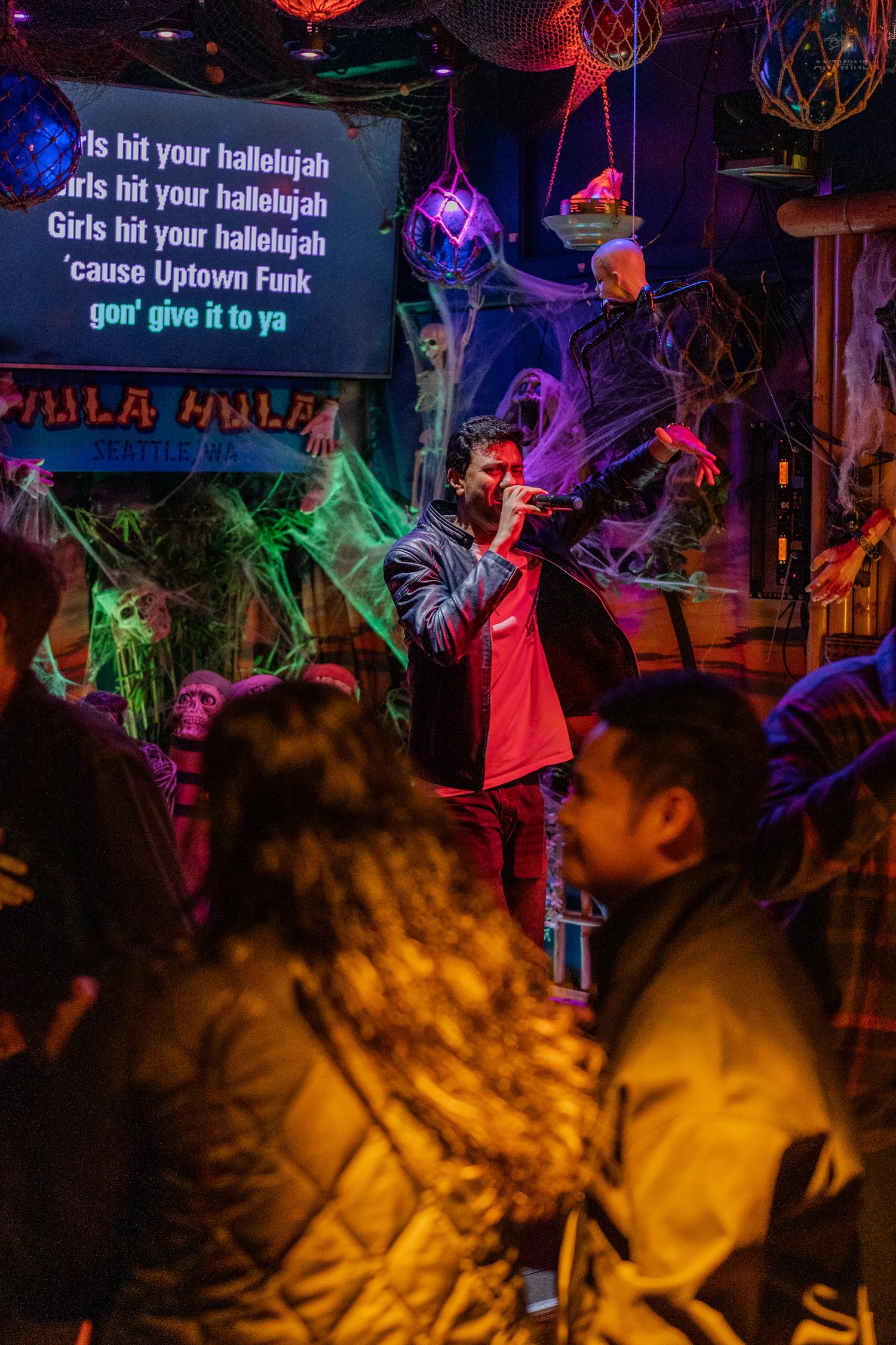 Man in red jacket performing Uptown Funk karaoke on a crowded Halloween-themed stage.