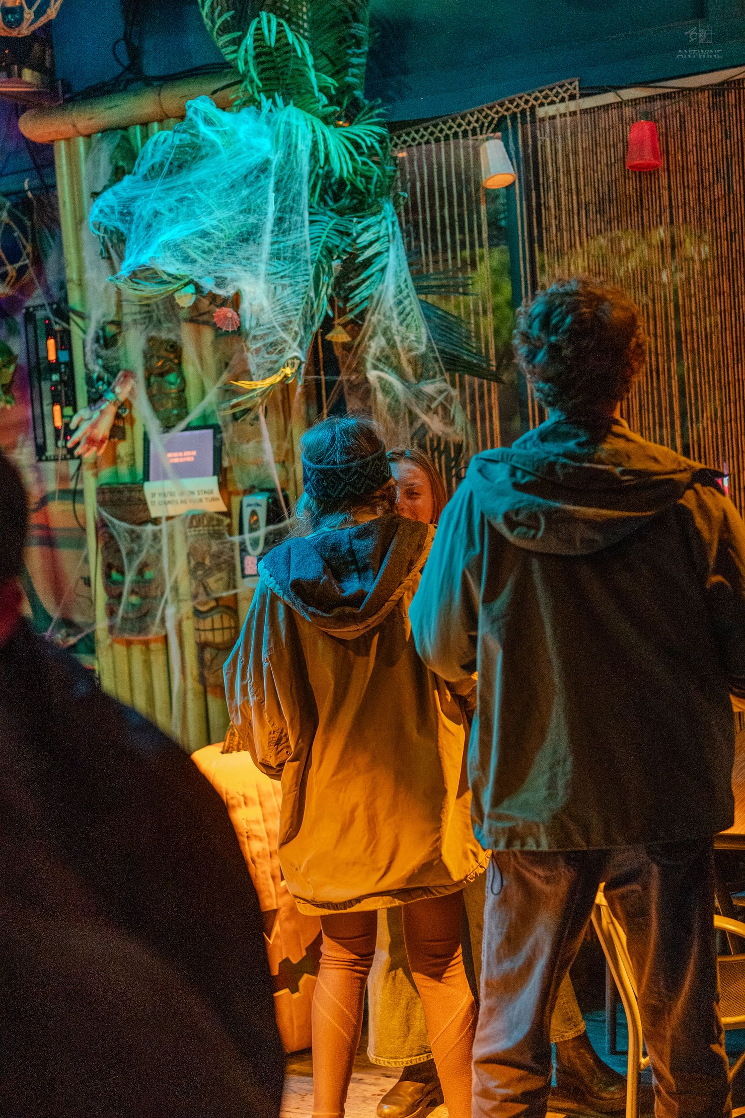 Couple viewing Halloween decorations with glowing teal cobwebs at a festively decorated bar.