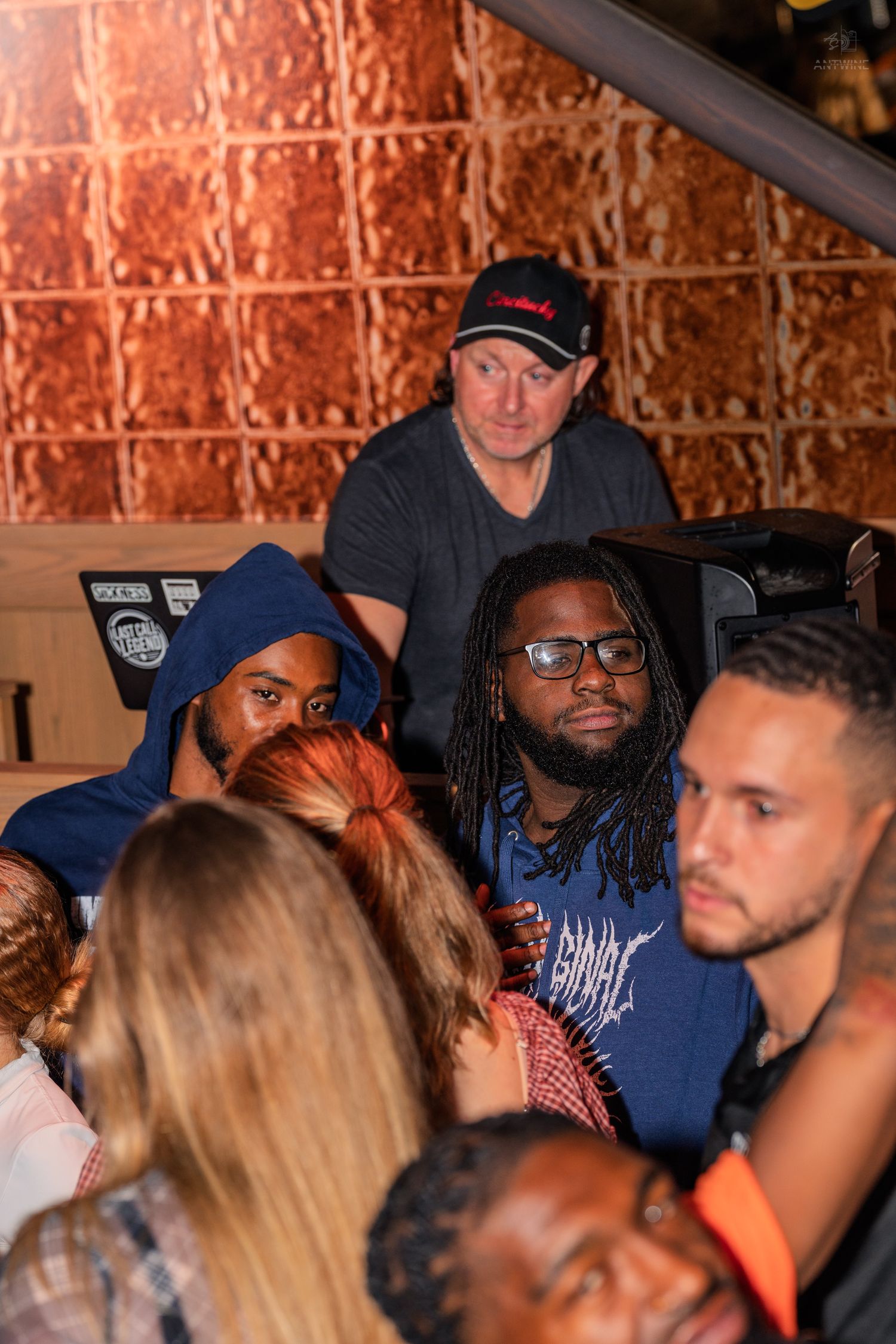 Diverse group of people gathered at a lively indoor bar event with brick wall backdrop.