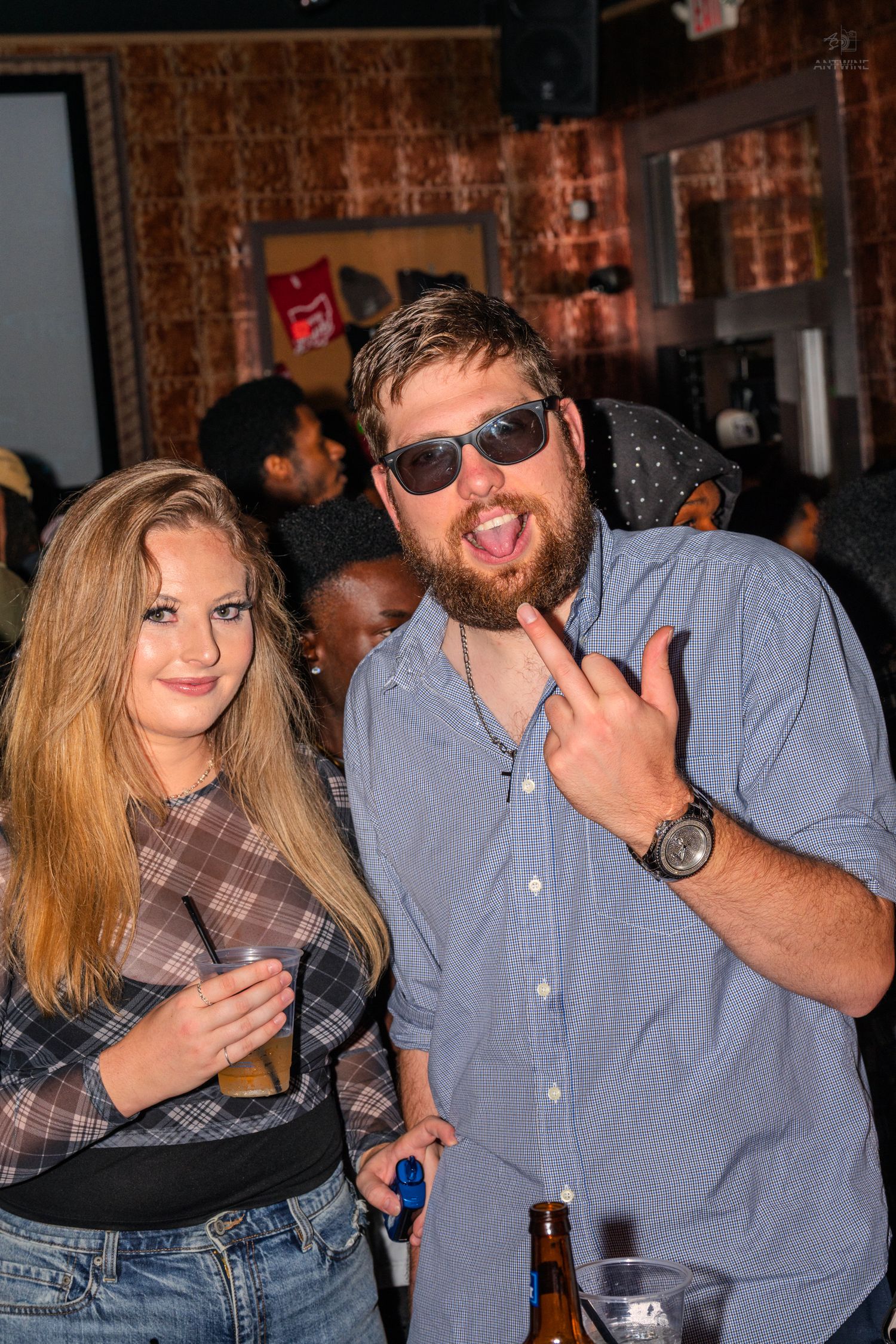 Smiling couple posing together at a bar, man making rock sign with sunglasses.