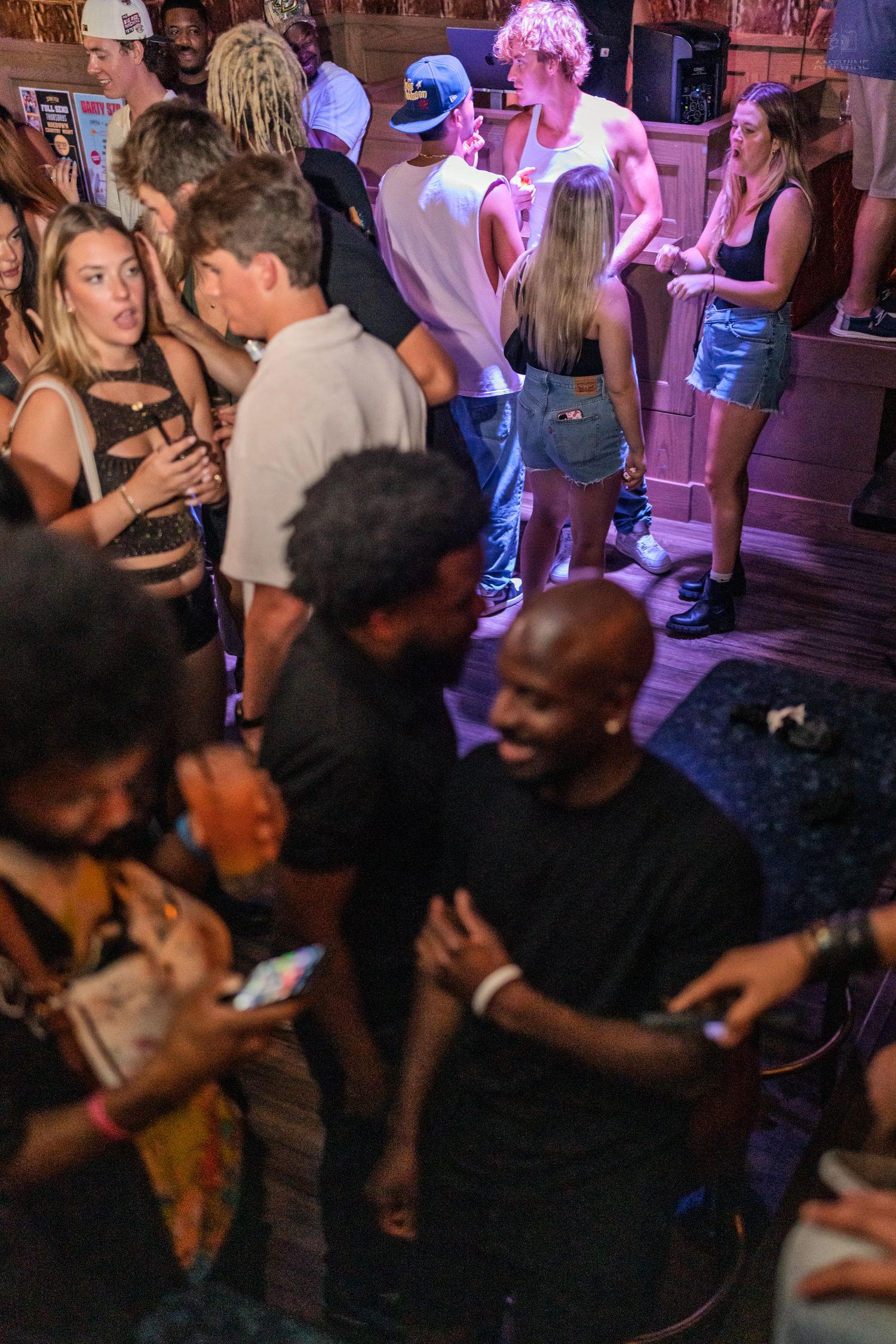 Energetic crowd dancing and socializing under purple lights at a packed nightclub venue.