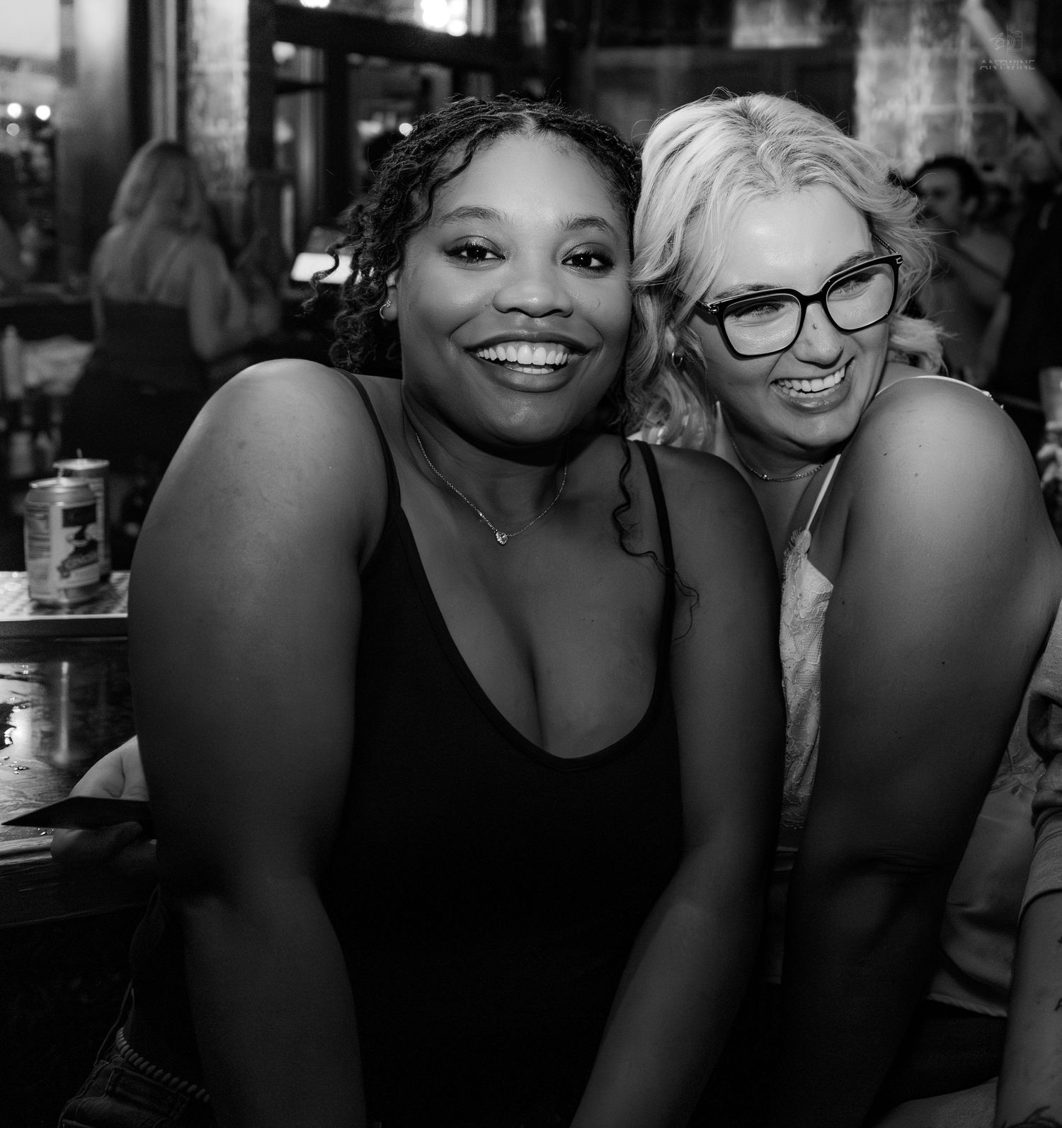 Two smiling women pose together at a bar in this black and white nightlife photo.