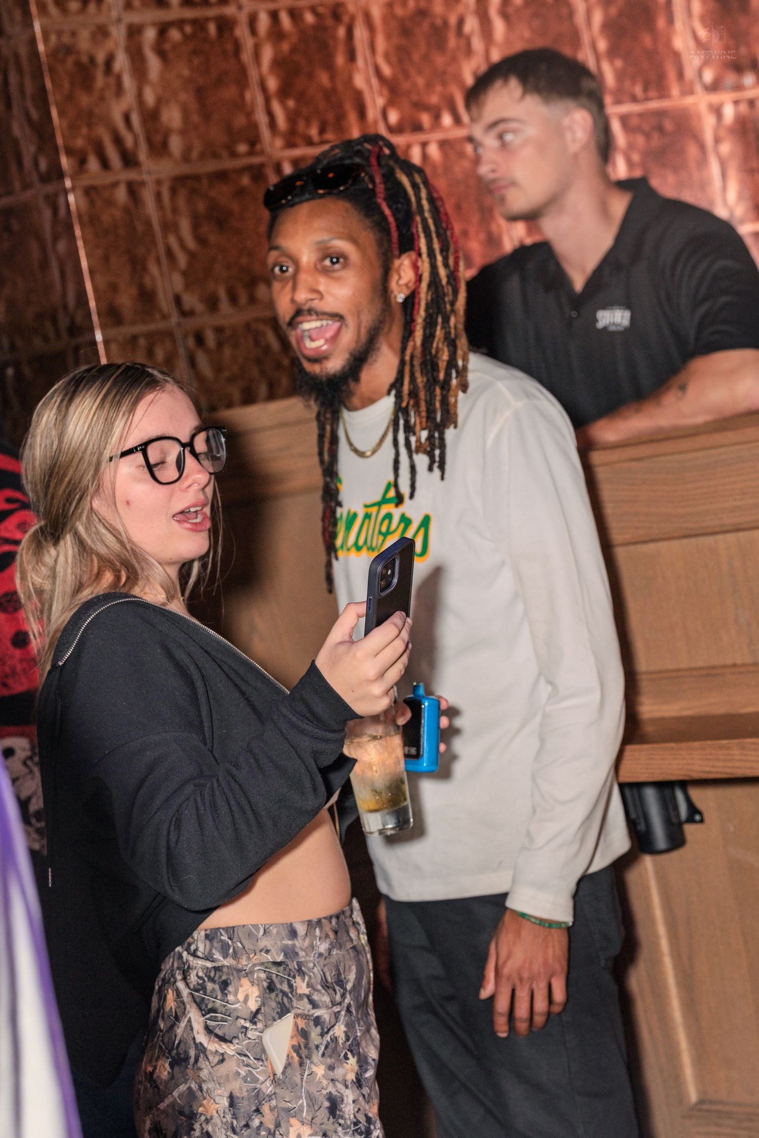 Blonde woman with glasses taking a selfie with a man with red dreadlocks at a party.
