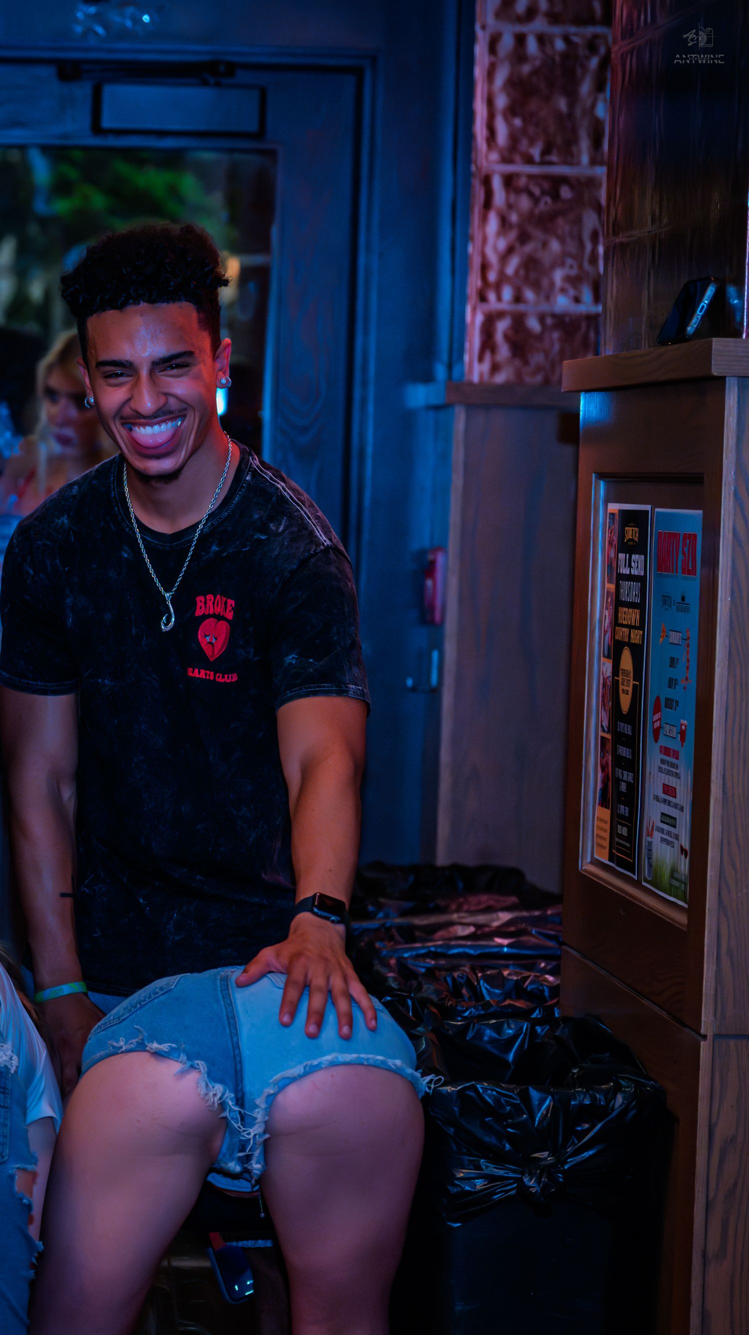 Young man smiling and laughing while sitting at a lively indoor venue at night.