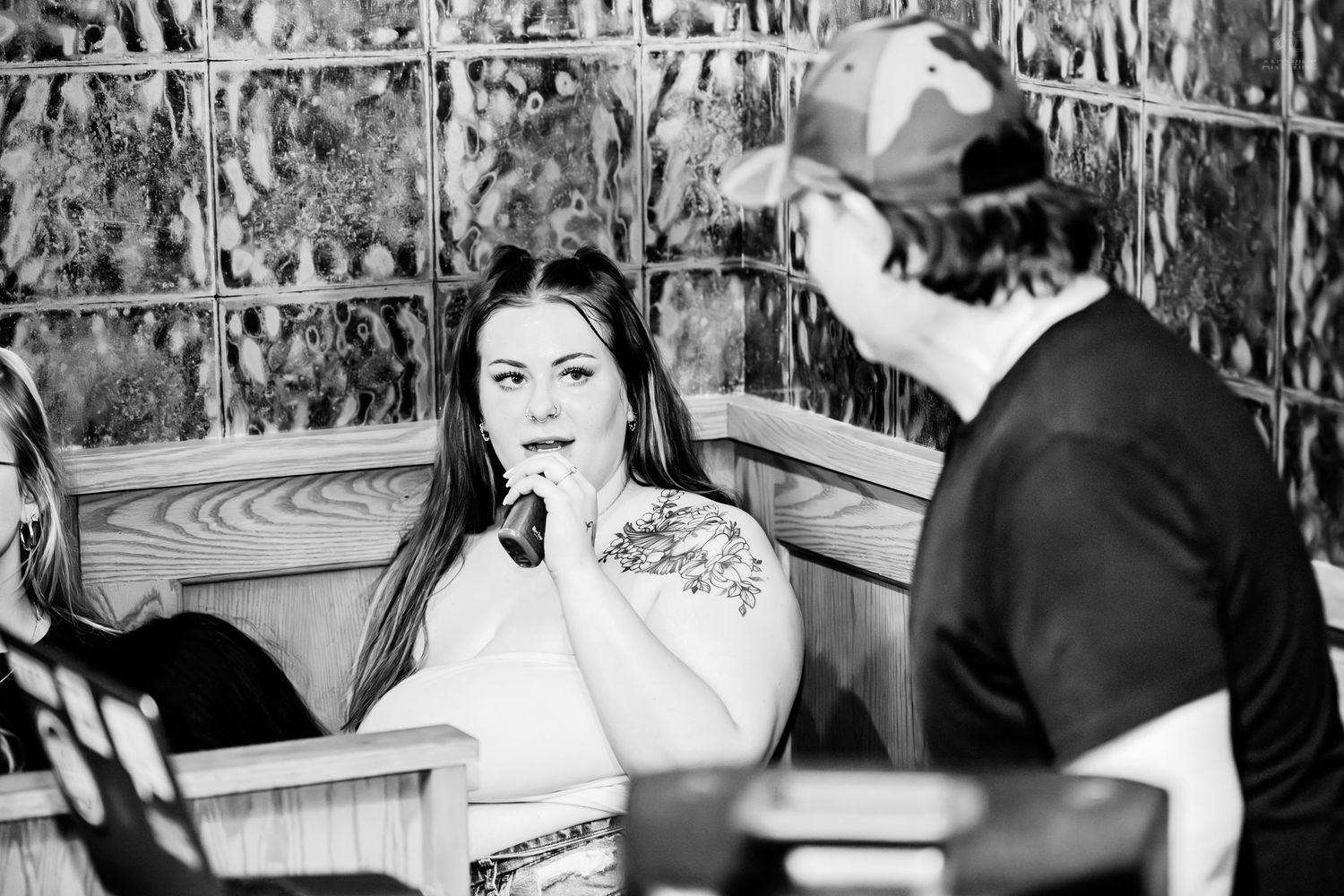 Black and white photo of tattooed woman listening to man at indoor venue.