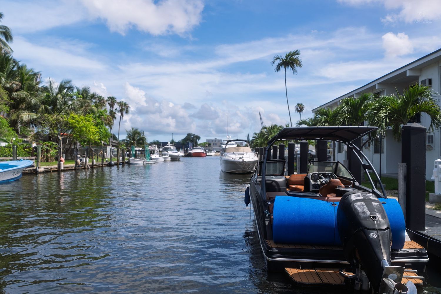 Black motorboat docked along a serene Florida canal lined with palm trees and waterfront homes.