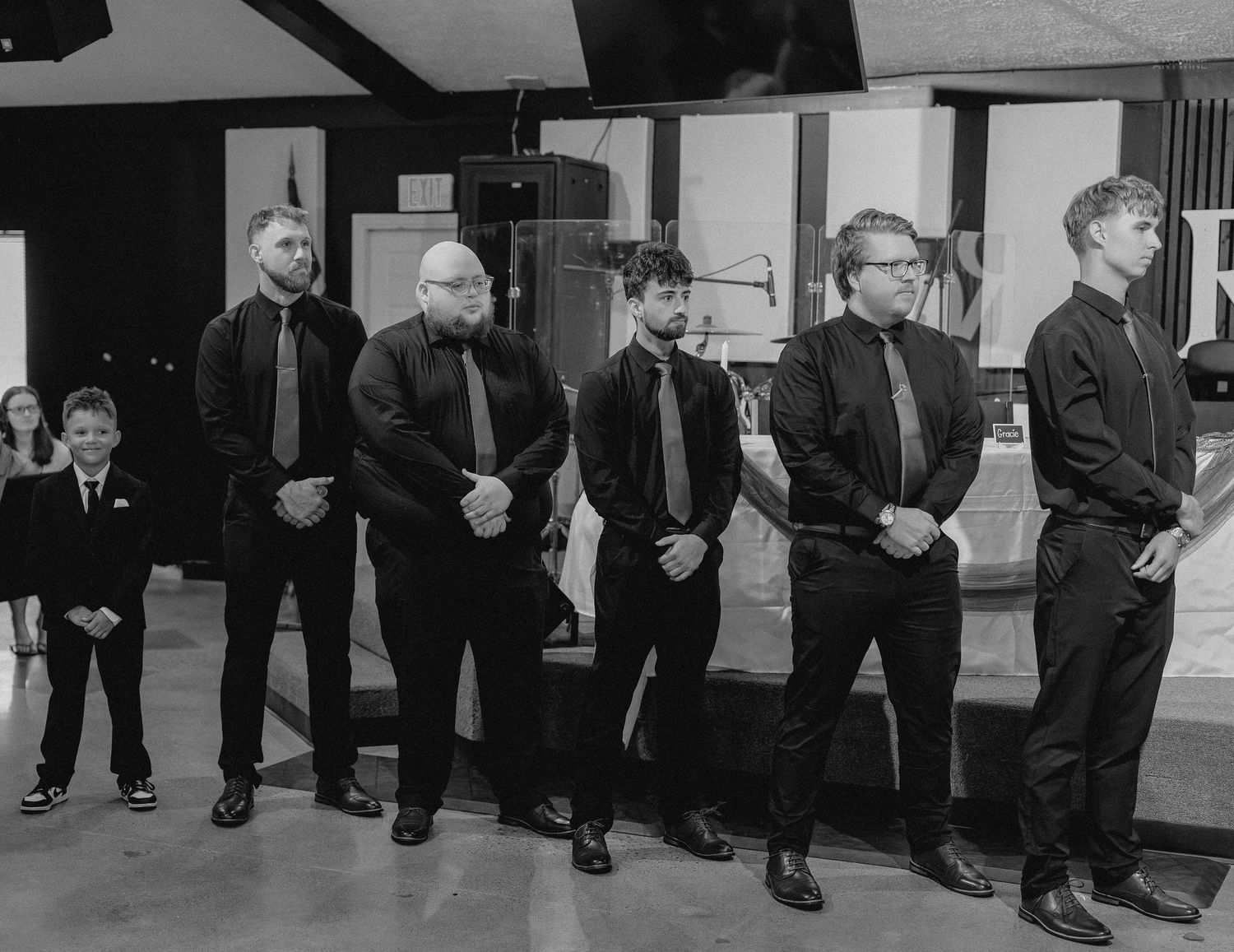 Black and white photo of groomsmen and a young boy in suits standing in a line at a wedding ceremony.