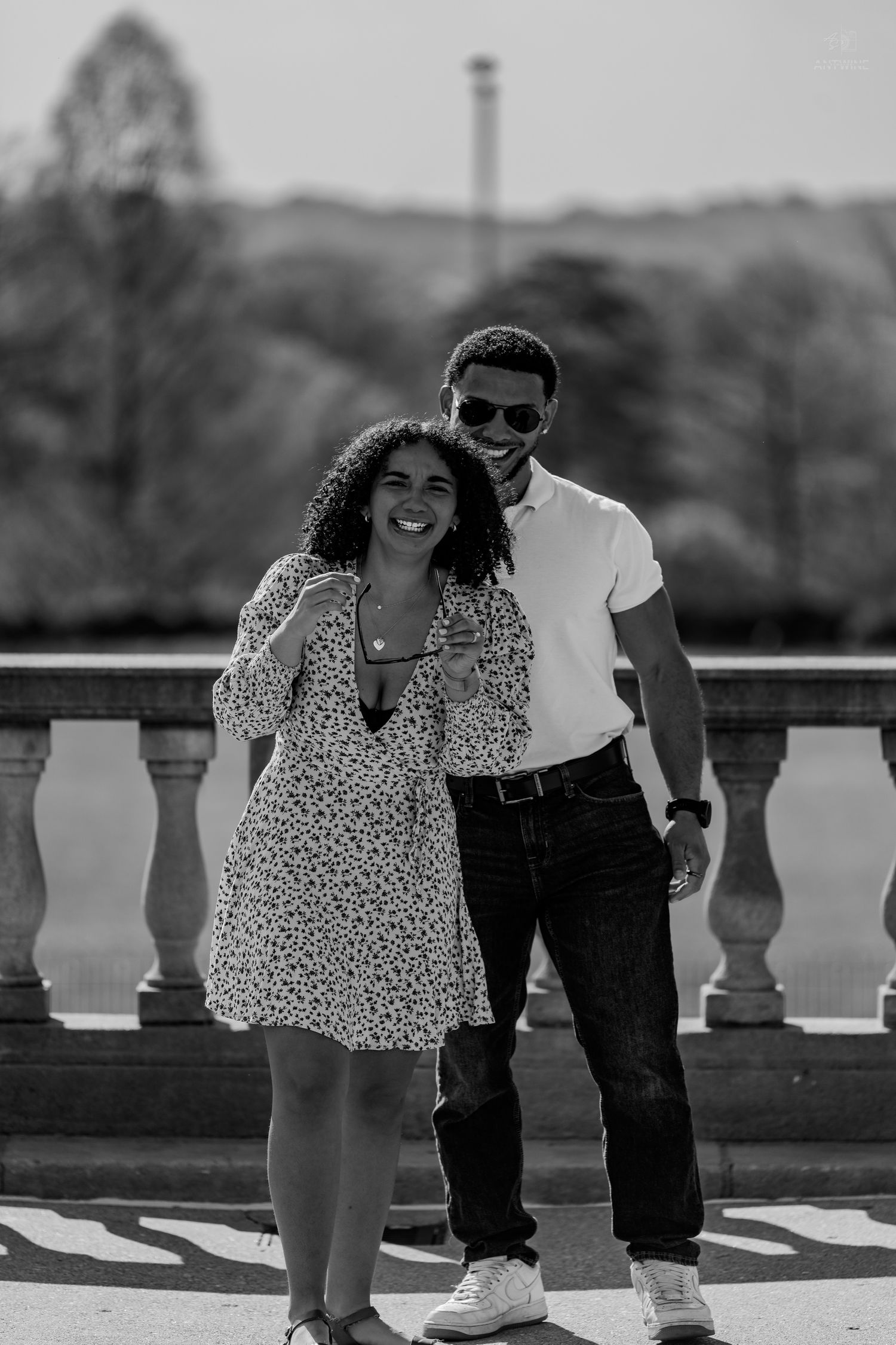 Black and white portrait of a smiling couple posing closely together on a sunny stone terrace.