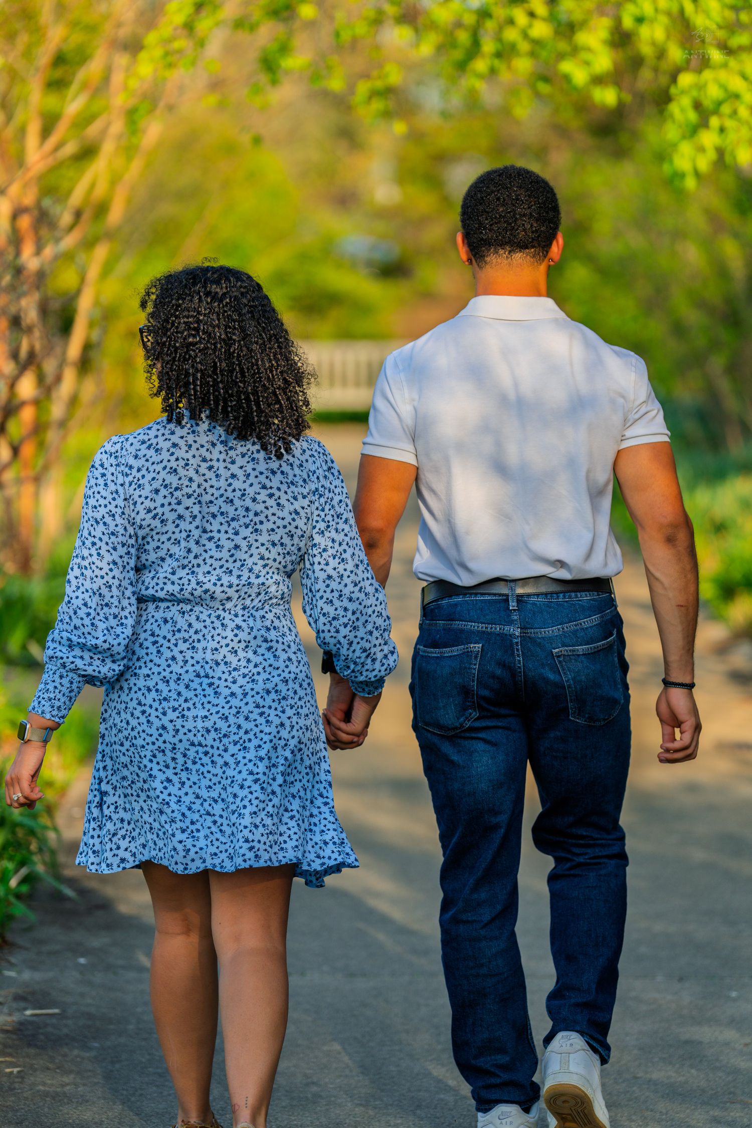 Rear view of a couple holding hands walking along a lush green park pathway in warm golden light.