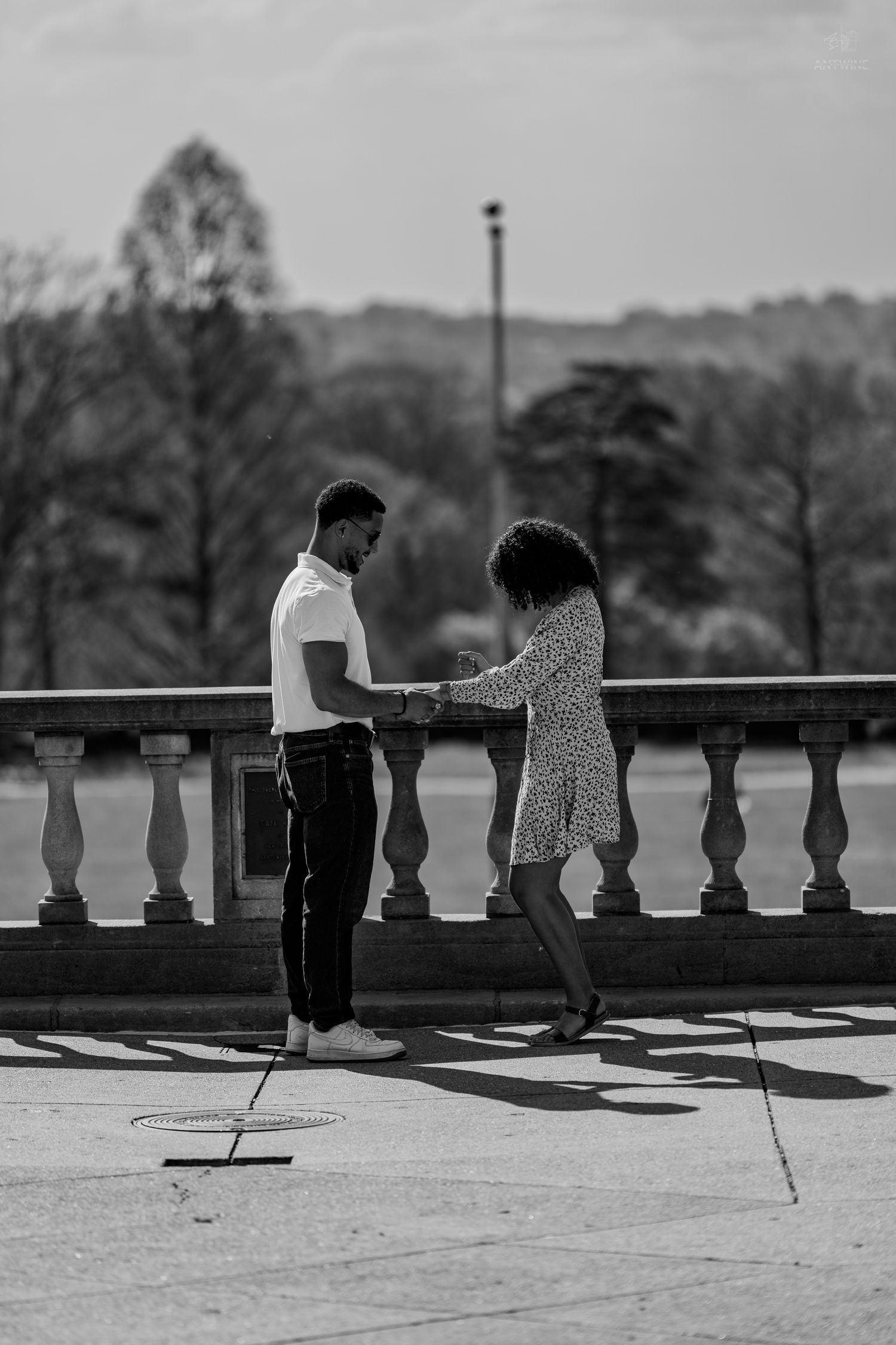 Black and white photo of couple dancing and holding hands on a stone terrace in a park.