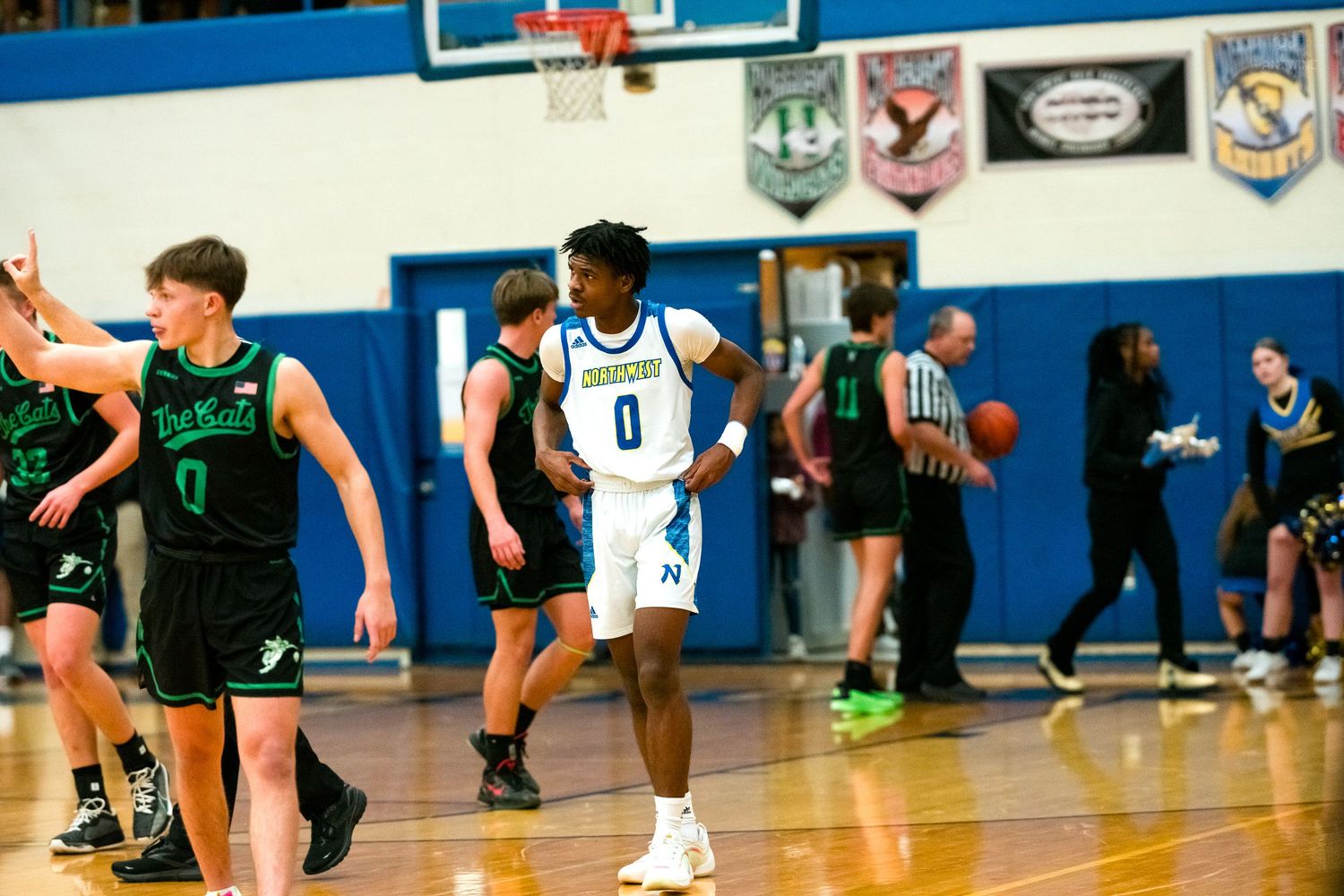 High school basketball player number 0 in white uniform celebrates on court during game against green-uniformed opponents.